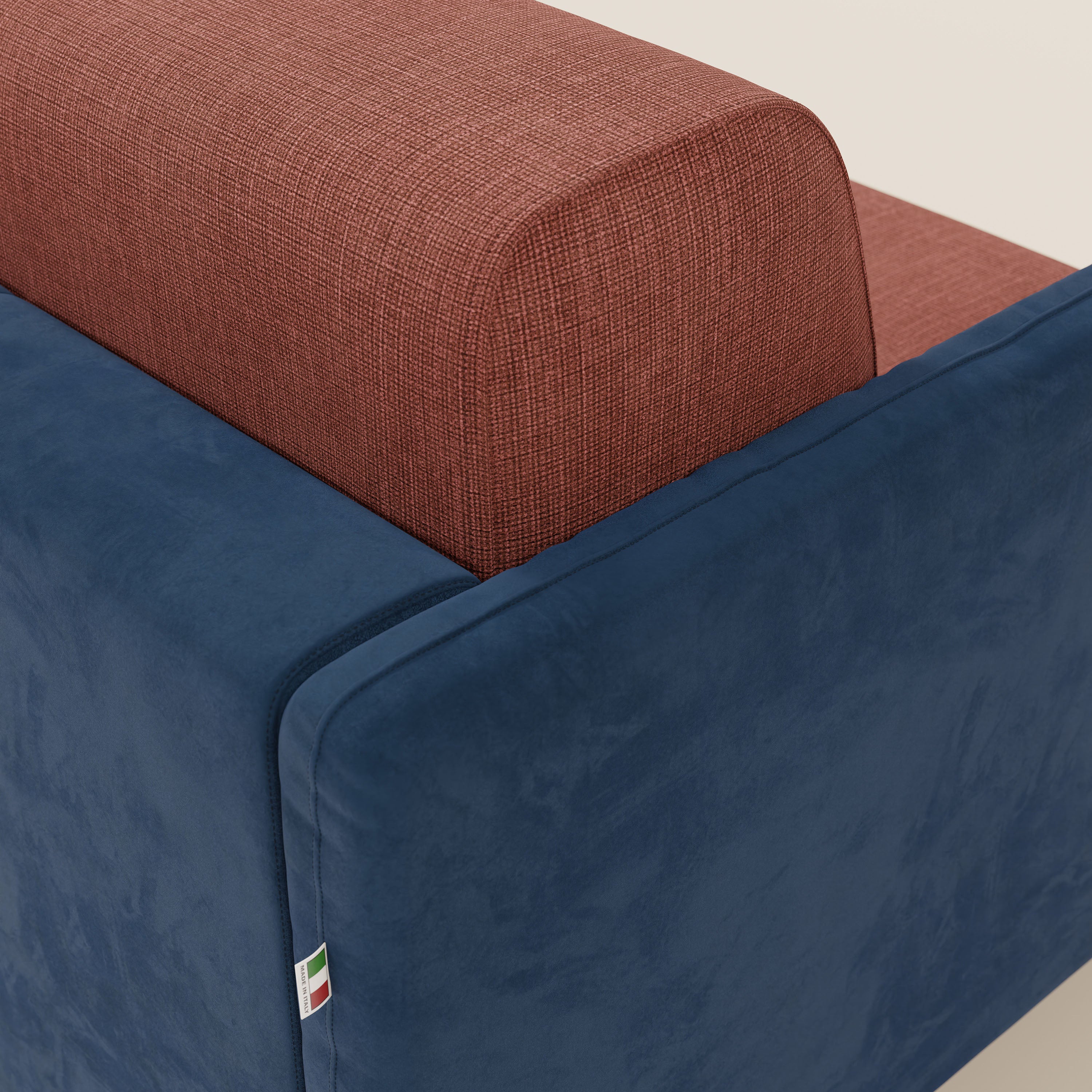 Un primo piano del divano letto Narciso di Divani.Store mostra lo schienale in corallo testurizzato e la base liscia T06 blu in microfibra antimacchia con tessuto impermeabile. Una targhetta con la bandiera italiana è cucita nella cucitura; lo sfondo è semplice e neutro.