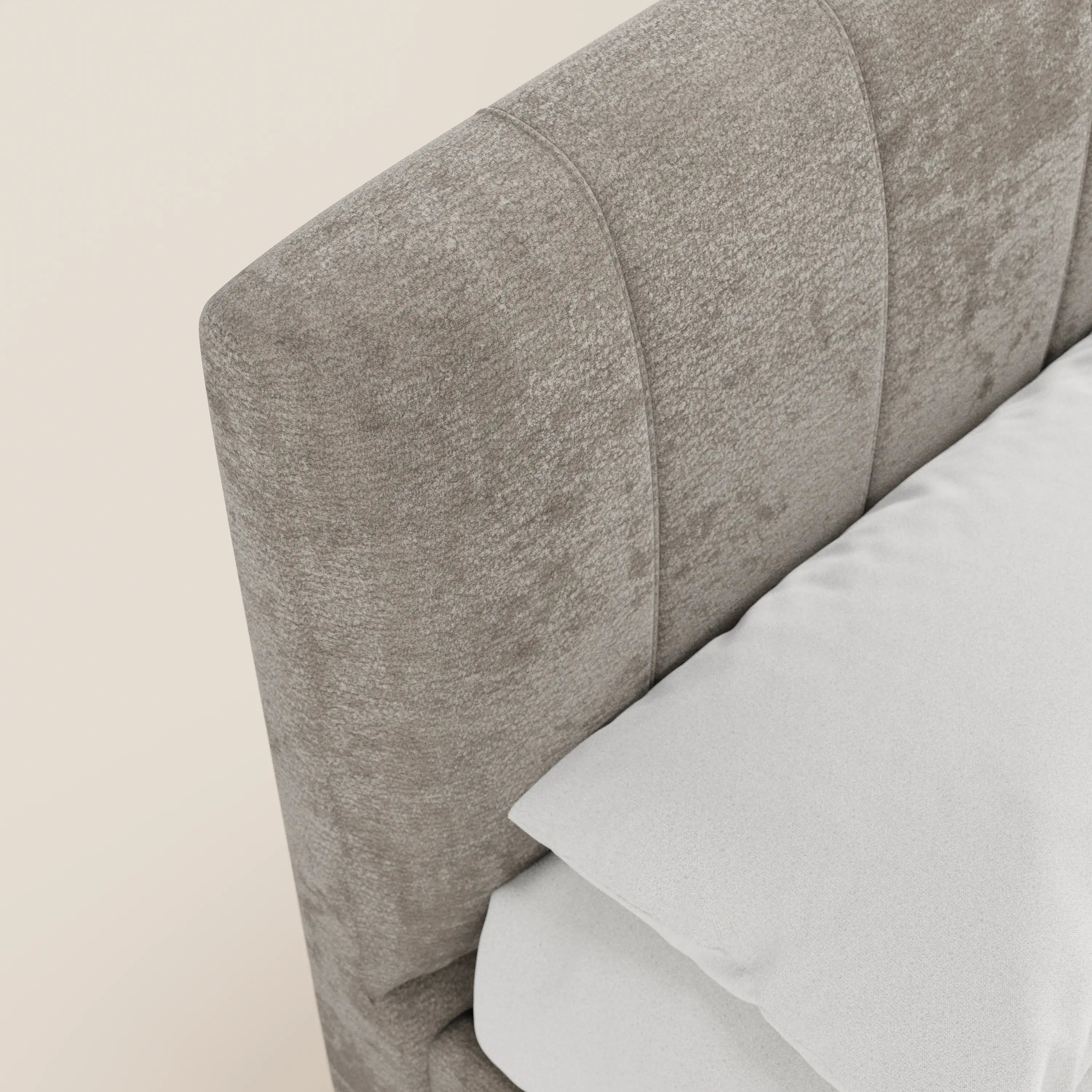 Primo piano del letto imbottito con contenitore ONYX di Letti.store, caratterizzato da una testiera in tessuto grigio chiaro certificato Oeko-Tex® con cuciture verticali. Il cuscino e il lenzuolo bianchi spiccano sul lato dello letto, sullo sfondo di una parete color crema, creando un look moderno e minimalista.