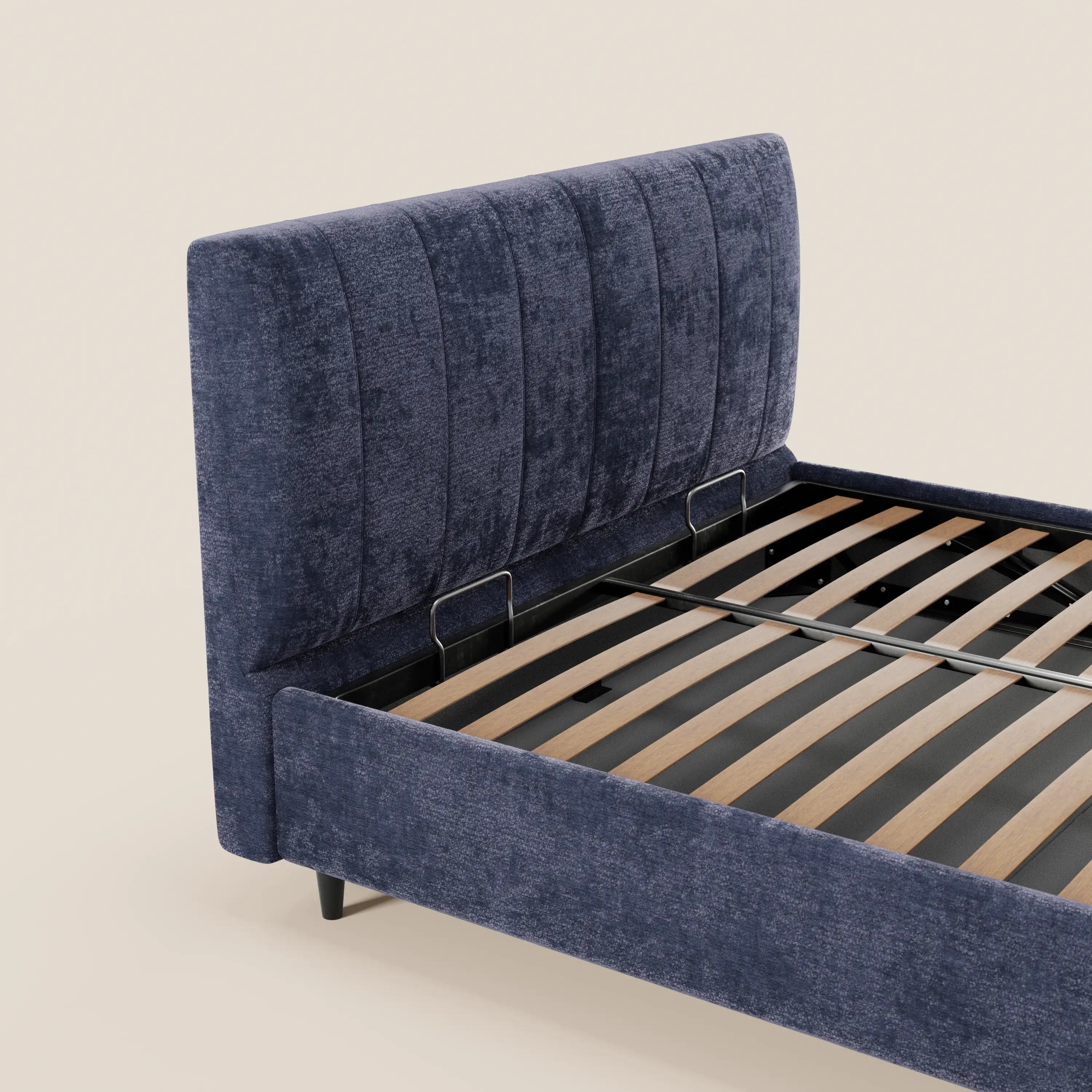 Il letto imbottito con contenitore ONYX di Letti.store presenta una testiera alta e verticale in tessuto blu scuro certificato Oeko-Tex® e fianchi rivestiti in tessuto, con doghe in legno e supporti in metallo nero; nella foto è raffigurato senza materasso su uno sfondo beige.