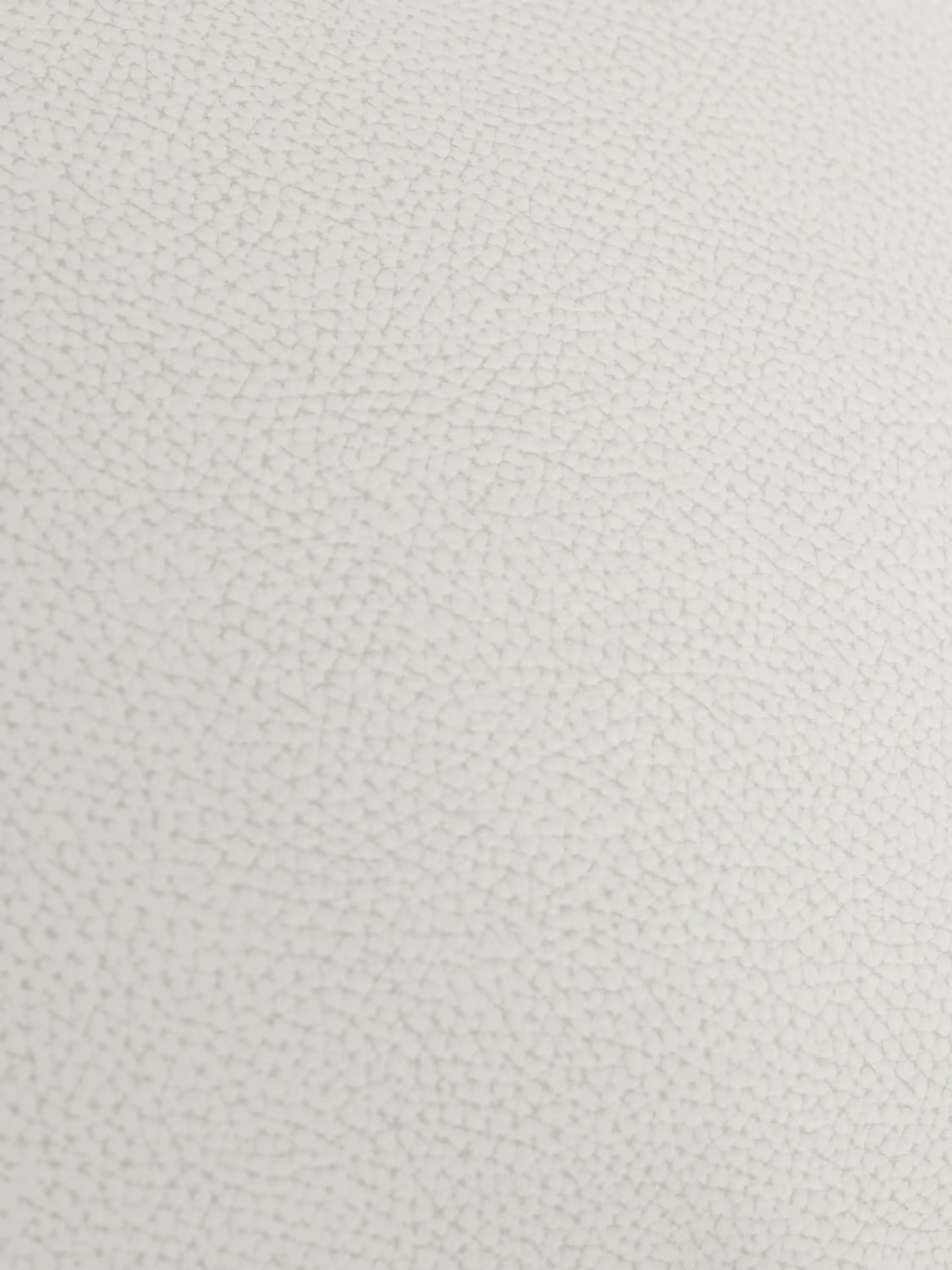 Primo piano della superficie color beige chiaro e dalla trama raffinata della poltrona Chester di Divani.Store, realizzata in vera pelle spessorata con capitonné artigianale, che mette in risalto la pelle genuina con una caratteristica grana irregolare simile a ciottoli, distribuita uniformemente su tutto il rivestimento. L'illuminazione soffusa accentua la delicata trama artigianale.