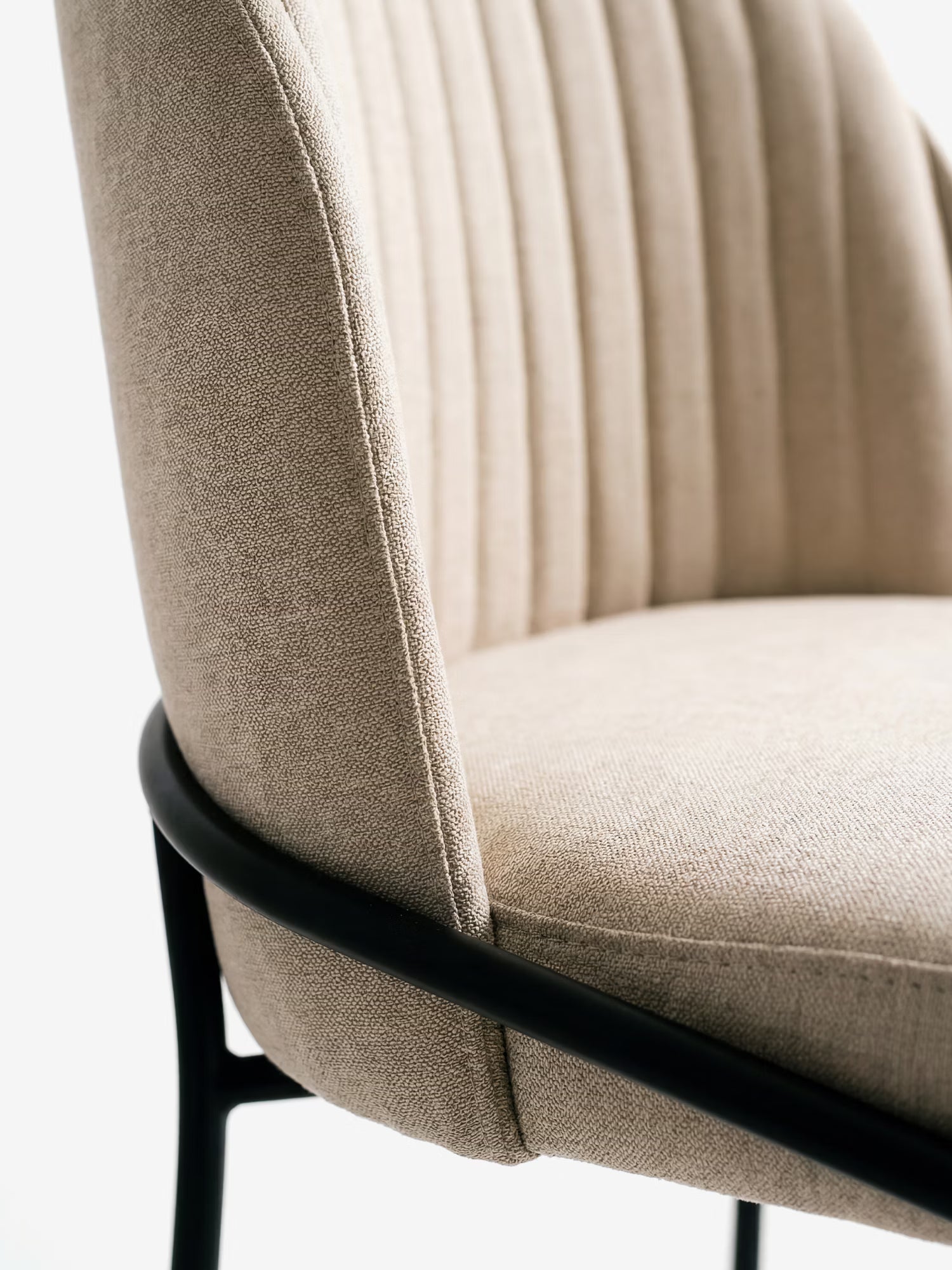 Primo piano della sedia imbottita “Plissè” di Divani.Store, caratterizzata da un tessuto impermeabile beige chiaro, uno schienale plissettato con cuciture verticali ed eleganti gambe in metallo nero. Lo sfondo è bianco a tinta unita.
