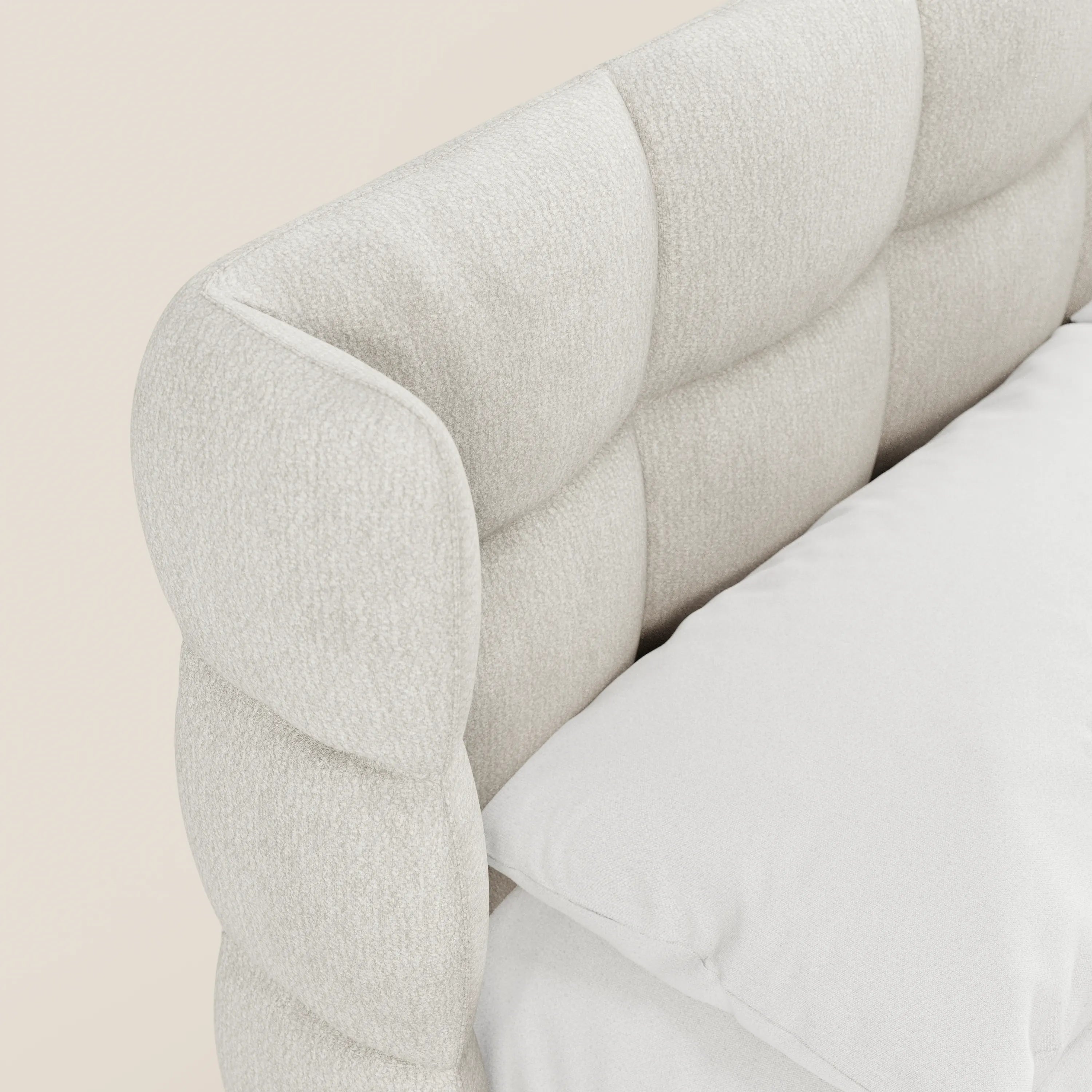 Primo piano del letto imbottito RAGNAR con contenitore e testiera capitonné avvolgente di Letti.store, realizzato in un elegante tessuto certificato Oeko-Tex®; presenta una testiera capitonné beige chiaro e un cuscino bianco su uno sfondo neutro.