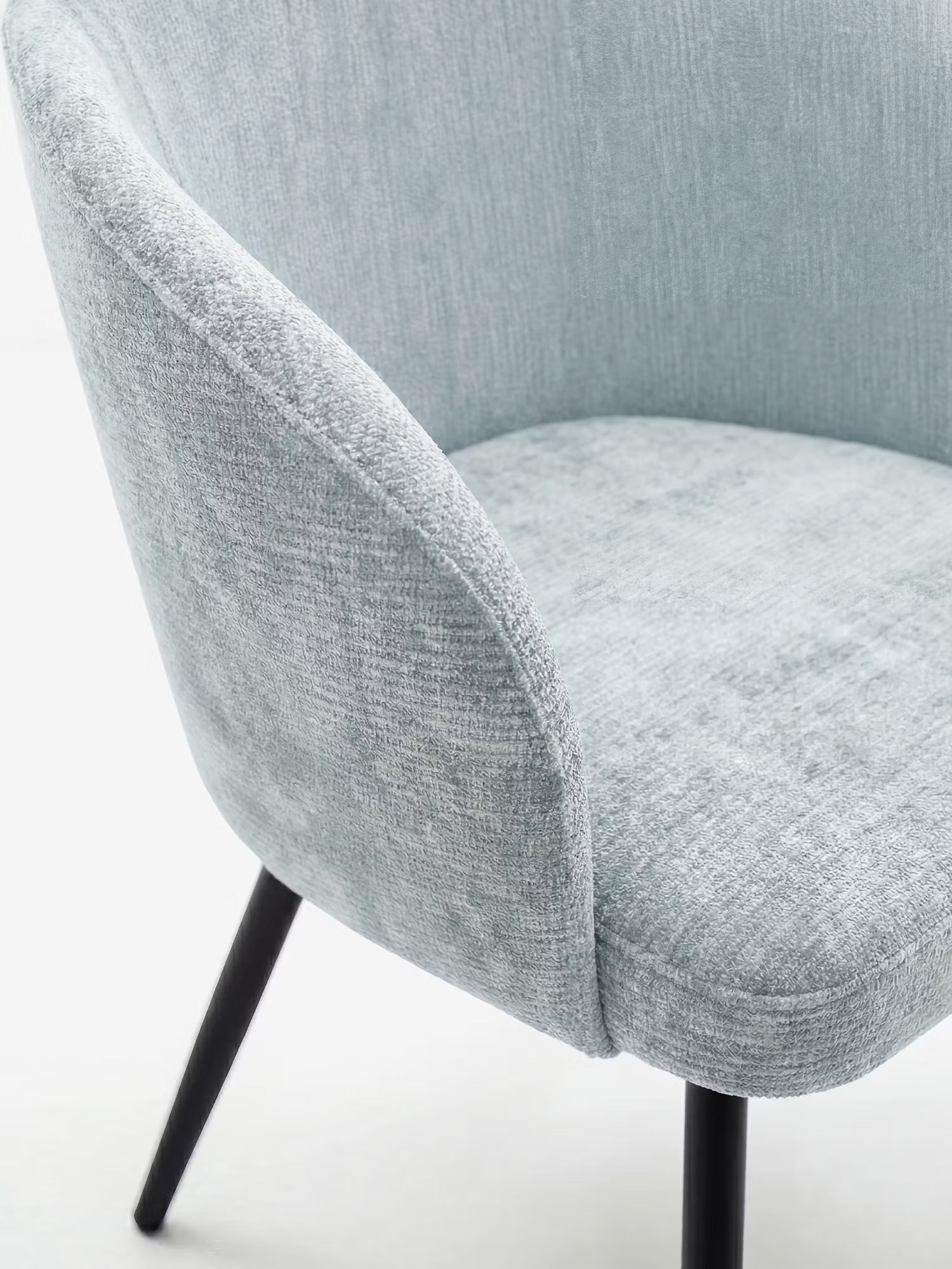 Primo piano della sedia Rovo con braccioli di Divani.Store: sedia moderna con schienale ricurvo, rivestimento imbottito in ciniglia grigio chiaro e sottili gambe in metallo nero, immortalata su uno sfondo bianco per un look elegante e minimalista.