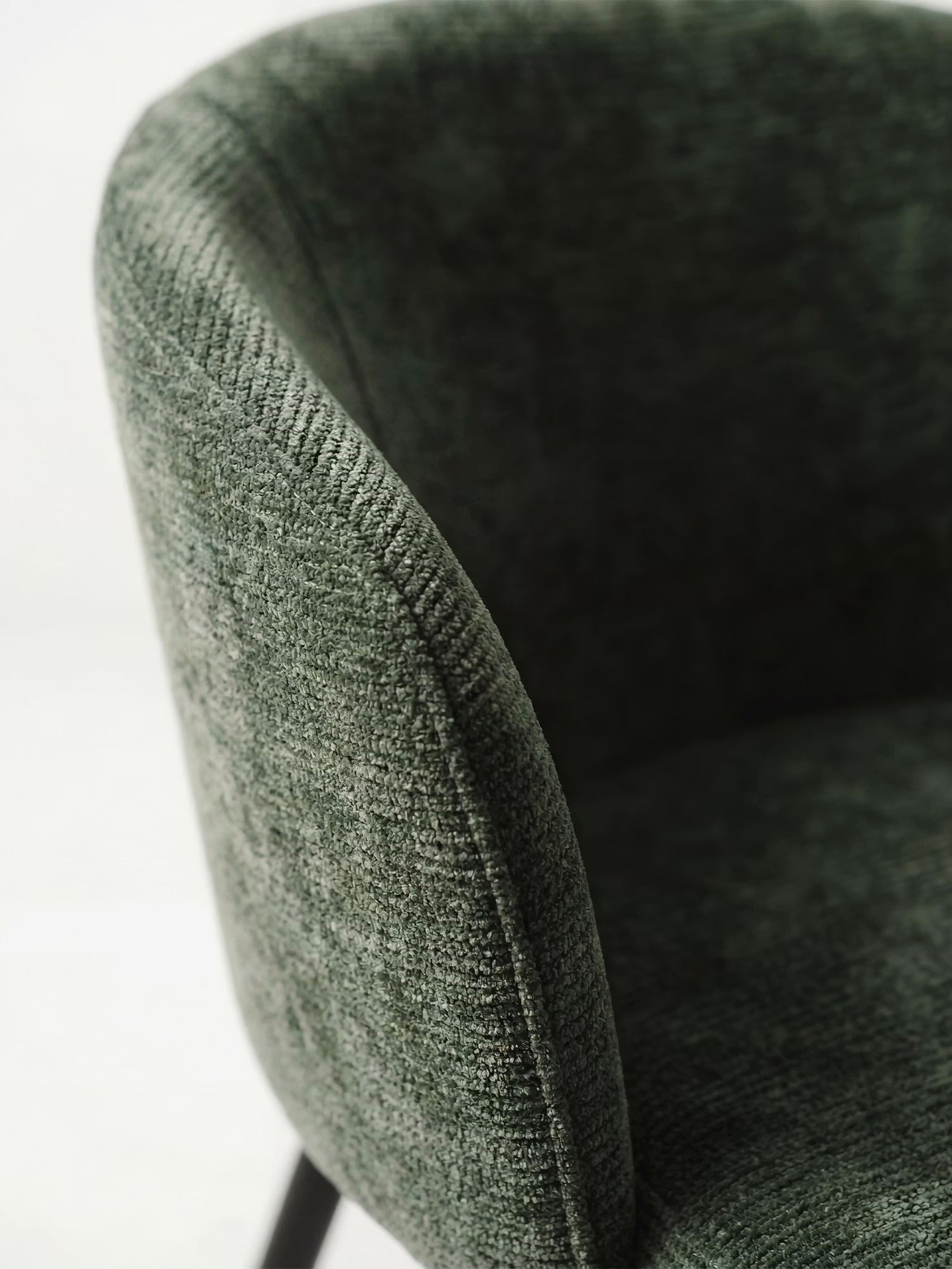 Primo piano della sedia Rovo con braccioli di Divani.Store, caratterizzata da un morbido rivestimento in ciniglia verde, uno schienale curvo e robuste gambe in metallo nero. Questa sedia imbottita moderna risalta su uno sfondo bianco.