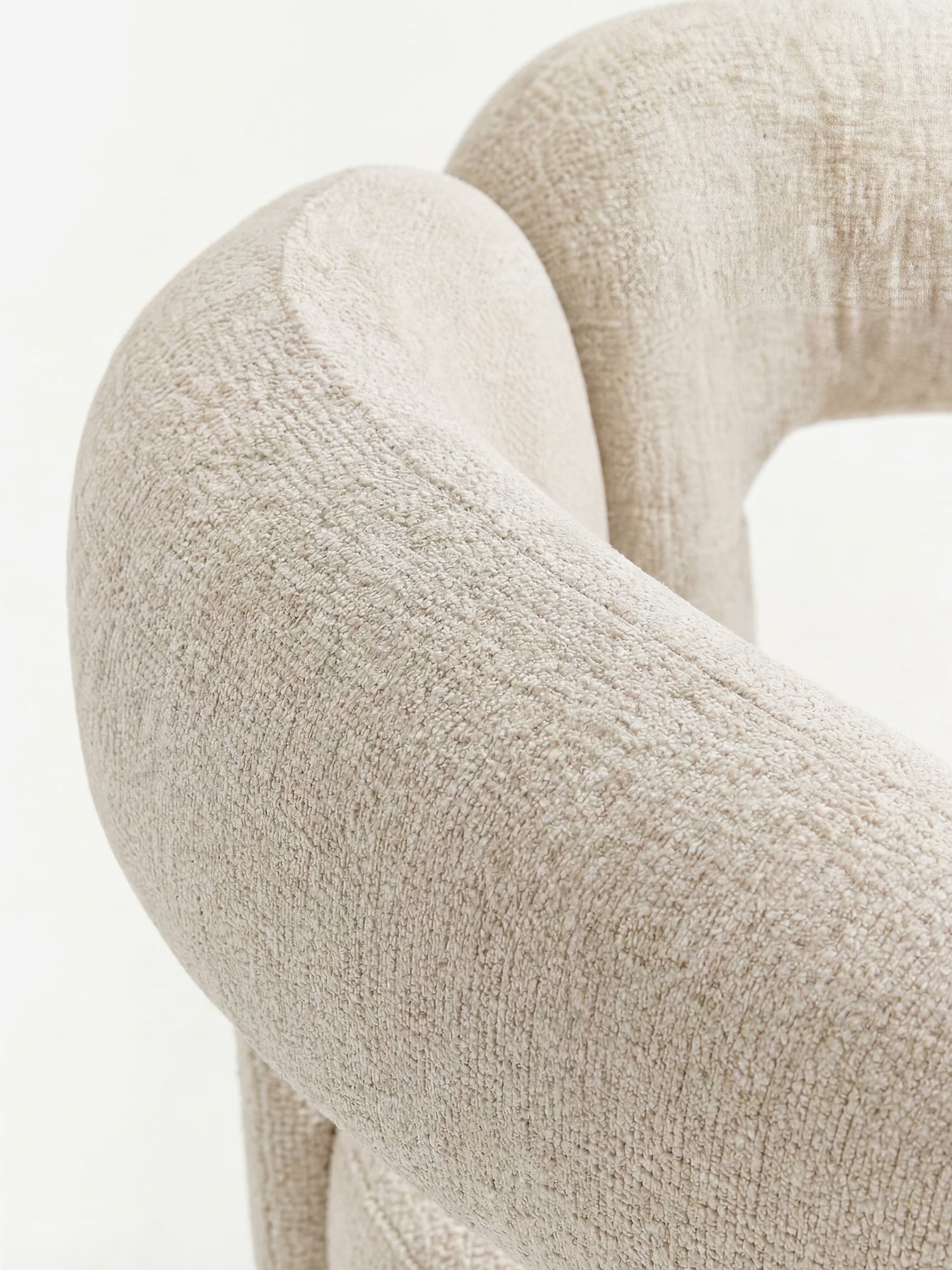 Primo piano della sedia di design “Sibilla” di Divani.Store, caratterizzata da una struttura ad arco interamente rivestita in beige chiaro. I braccioli imbottiti e lo schienale curvo mettono in risalto il suo tessuto morbido e il delicato motivo intrecciato, su uno sfondo leggermente sfocato.