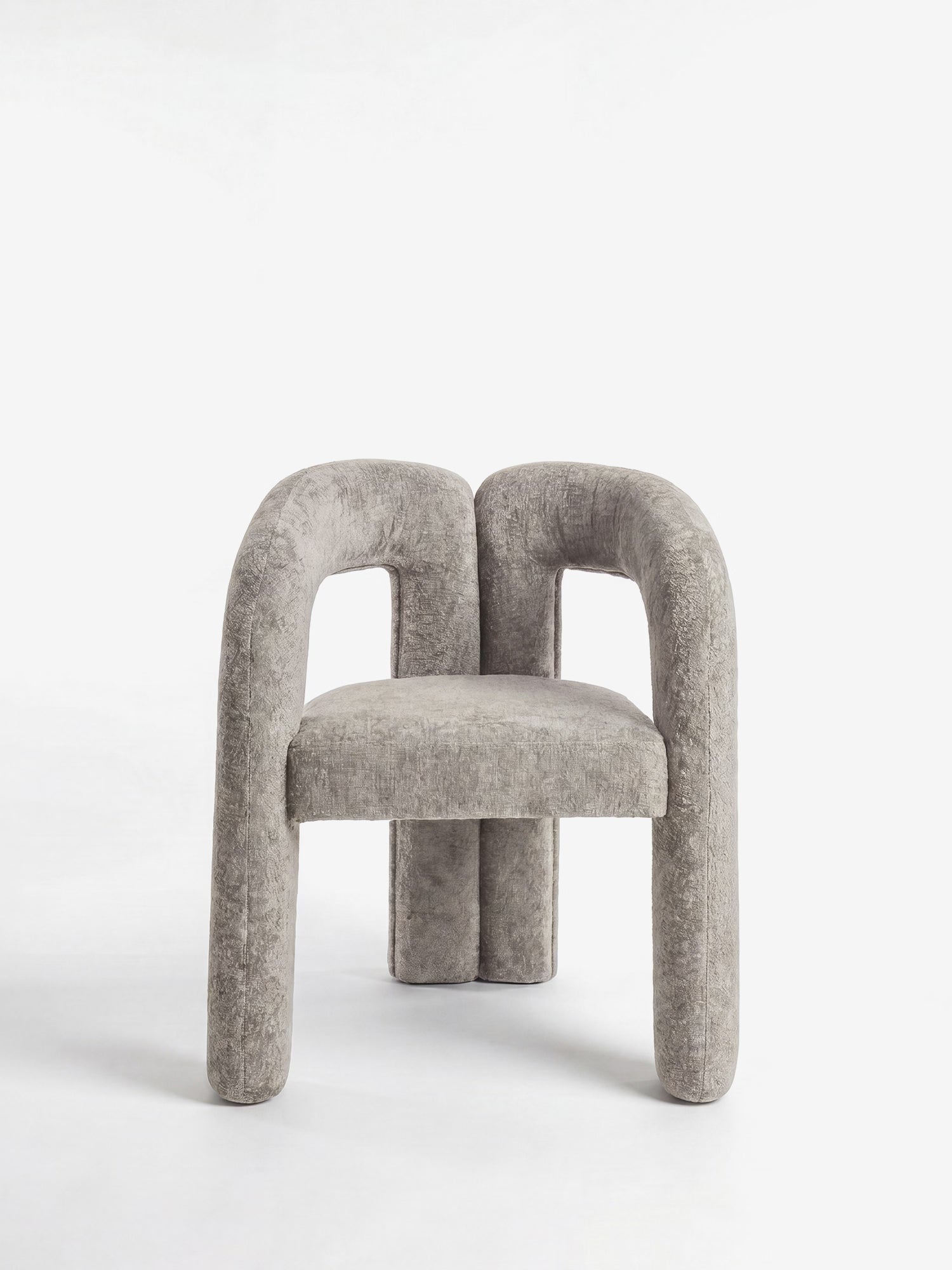 La Sibilla, sedia di design imbottita di Divani.Store, è caratterizzata da un morbido tessuto grigio chiaro, gambe e braccioli tubolari arrotondati e un design minimalista e scultoreo. Lo sfondo bianco a tinta unita esalta la sua forma arcuata unica e lo stile moderno.