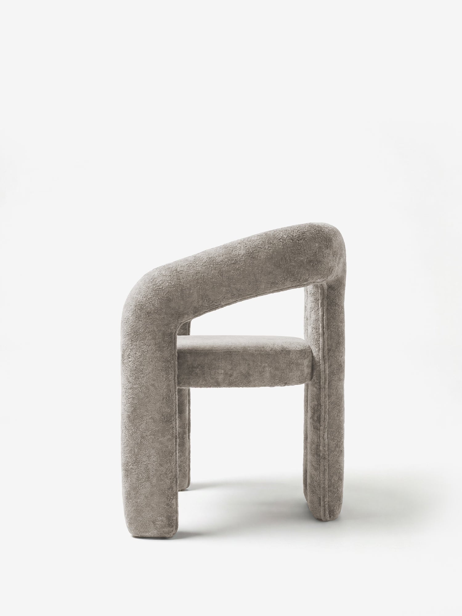 La sedia di design Sibilla di Divani.Store è una sedia moderna, interamente imbottita in tessuto grigio, con una struttura arcuata e continua, priva di doghe o gambe visibili, raffigurata di profilo su uno sfondo bianco.