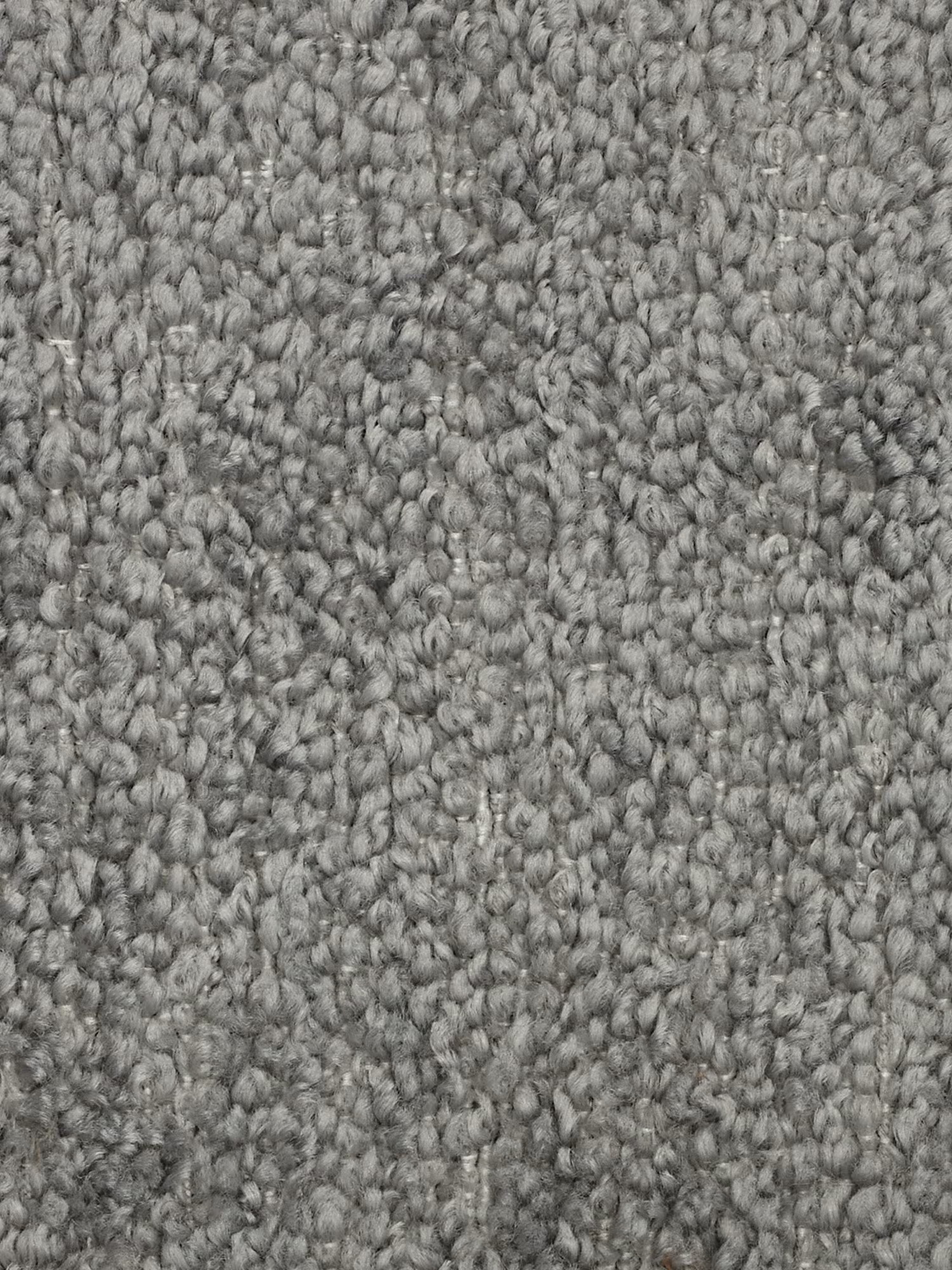 Primo piano di un tappeto grigio testurizzato con fibre a riccioli fitti. La superficie presenta un aspetto morbido e uniforme con sottili variazioni di colore, che vanno dal grigio chiaro al grigio scuro, creando profondità e un effetto leggermente screziato. Abbinato magnificamente alla poltrona Mosaic modulo da 77 cm in bouclé - capitonné e design in tessuto smacchiabile T21 di Divani.Store, il tappeto appare soffice e confortevole, perfetto per qualsiasi ambiente raffinato.