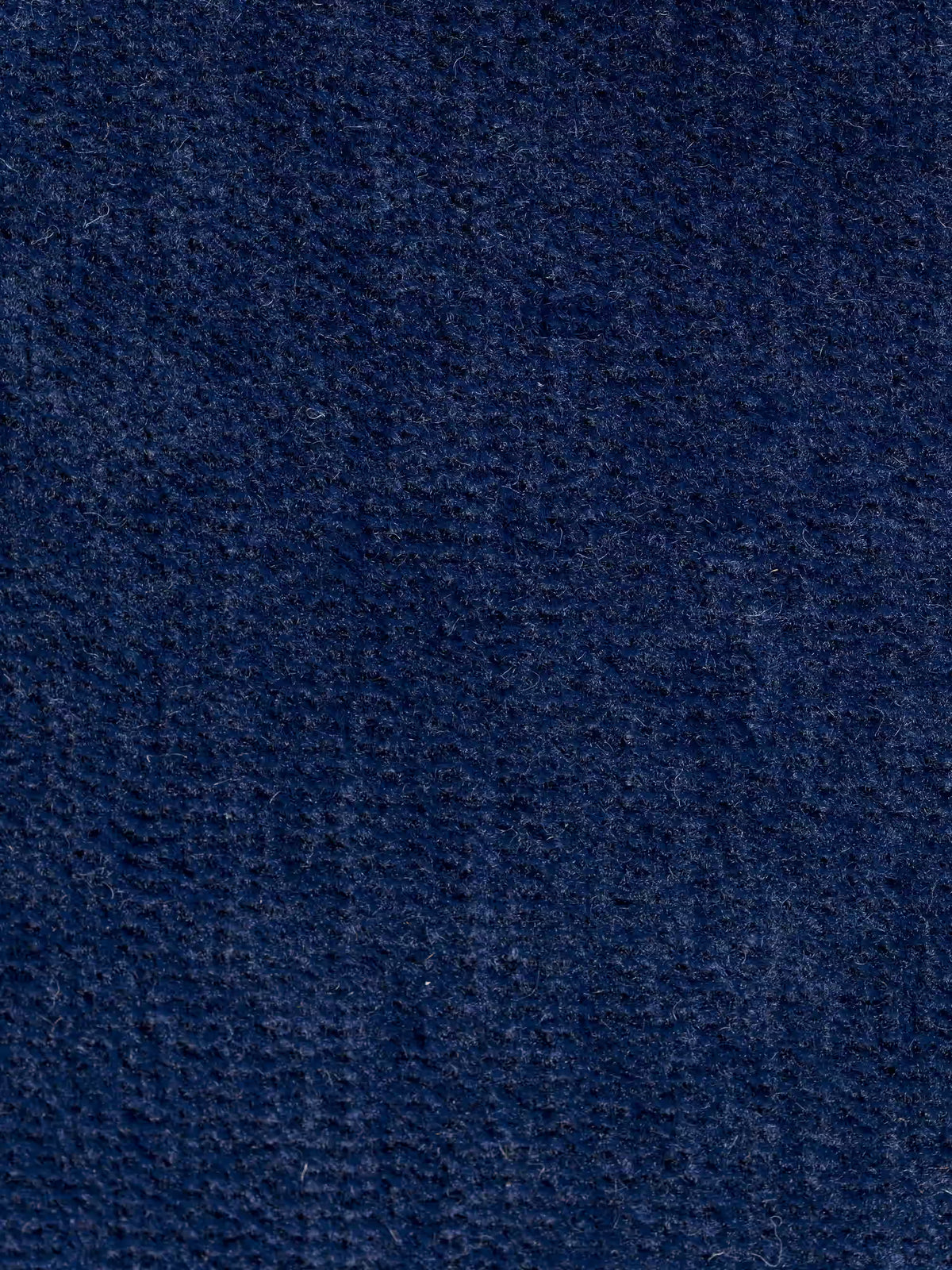 Primo piano della superficie testurizzata del divano angolare bicolore con penisola e base in metallo “Basalto” di Divani.Store, rivestito con il tessuto smacchiabile T31 in una ricca tonalità di blu navy. Le fibre a vista e l’aspetto leggermente irregolare, morbido e soffice evidenziano l’alta qualità del materiale e creano sottili variazioni nelle tonalità di blu alla luce, accentuando il suo design elegante con gli schienali imbottiti in piuma.