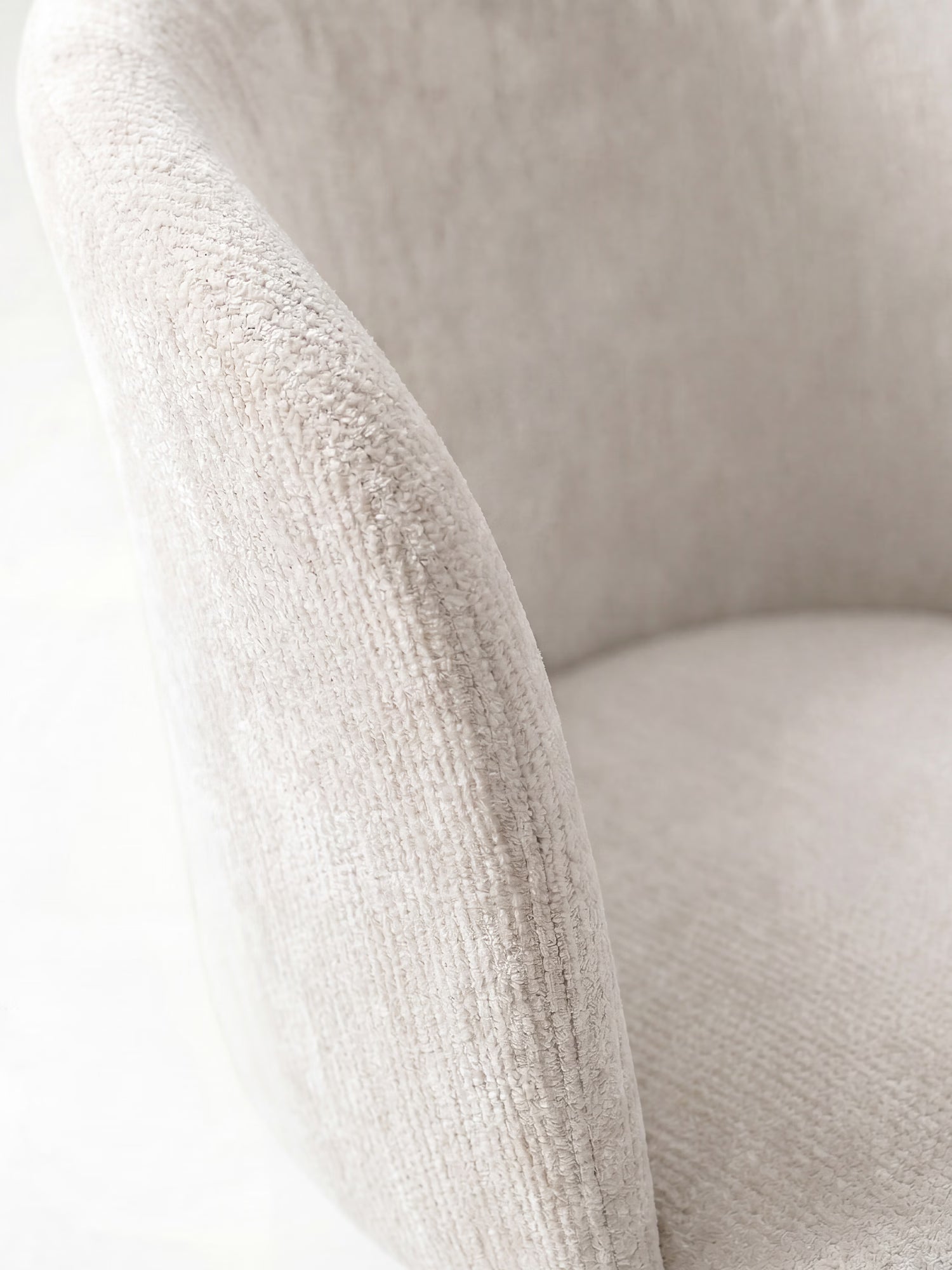 Primo piano della sedia moderna “Talia” di Divani.Store, rivestita in morbido tessuto ciniglia OEKO-TEX® color beige chiaro, con schienale e seduta curvi e imbottiti. La delicata trama del tessuto esalta il suo design elegante e accogliente. Lo sfondo è leggermente sfocato.
