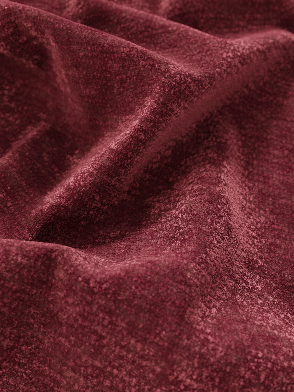 Un primo piano del tessuto color bordeaux intenso, dall’effetto vellutato, che riveste il letto imbottito ONYX con contenitore e testiera verticale, dove le delicate pieghe e le ombre mettono in risalto la consistenza morbida della testiera dallo schienale alto.
