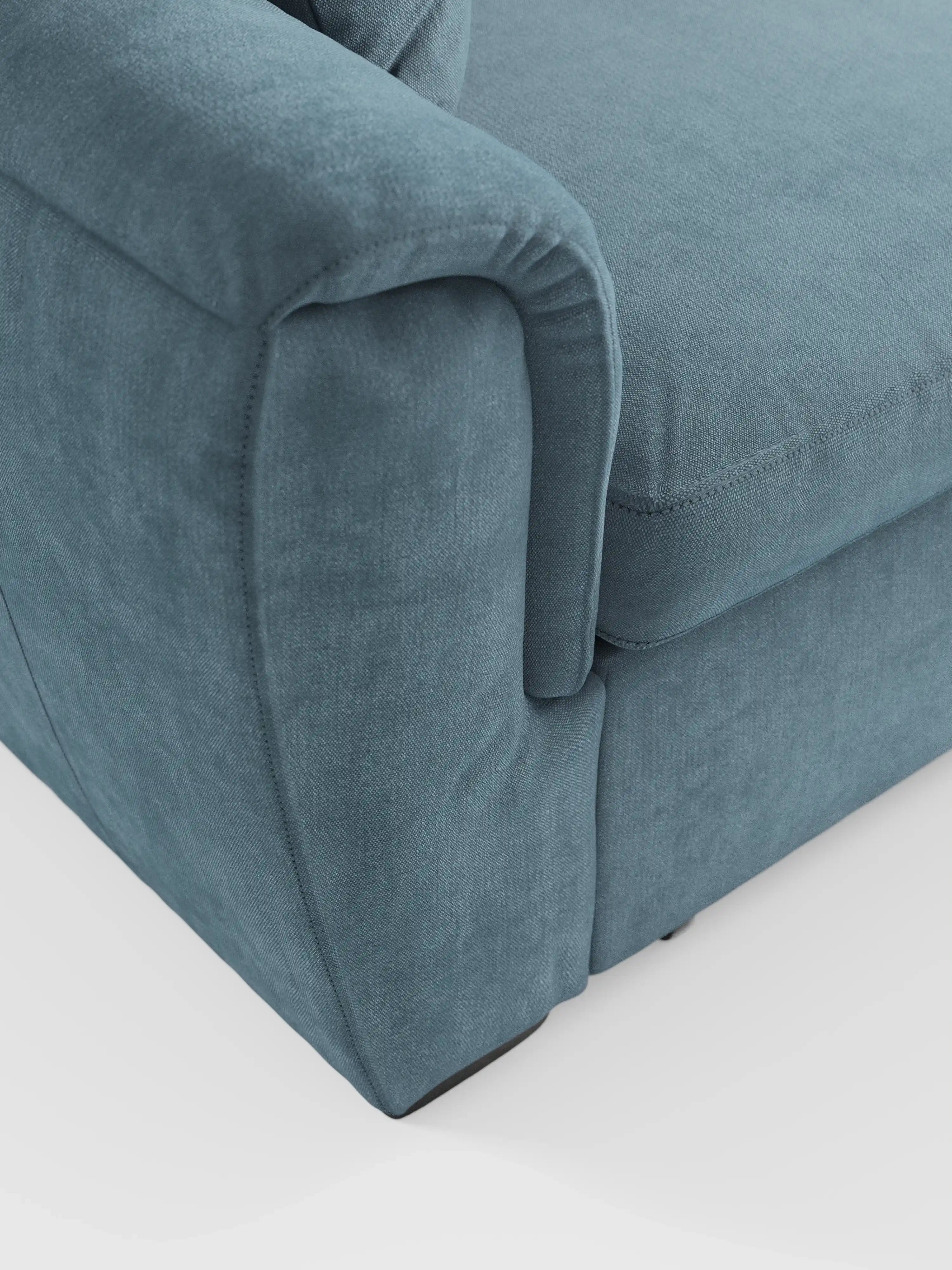 Primo piano dell'angolo del divano a 2 posti estraibile Titano di Divani.Store, con particolare attenzione al bracciolo, al cuscino di seduta e al pannello laterale. Questo divano in stile moderno è rivestito in morbido tessuto antimacchia certificato Oeko-Tex® con cuciture a vista lungo i bordi. Il suo design compatto con poggiatesta reclinabili lo rende ideale per qualsiasi ambiente, in particolare su uno sfondo bianco a tinta unita.
