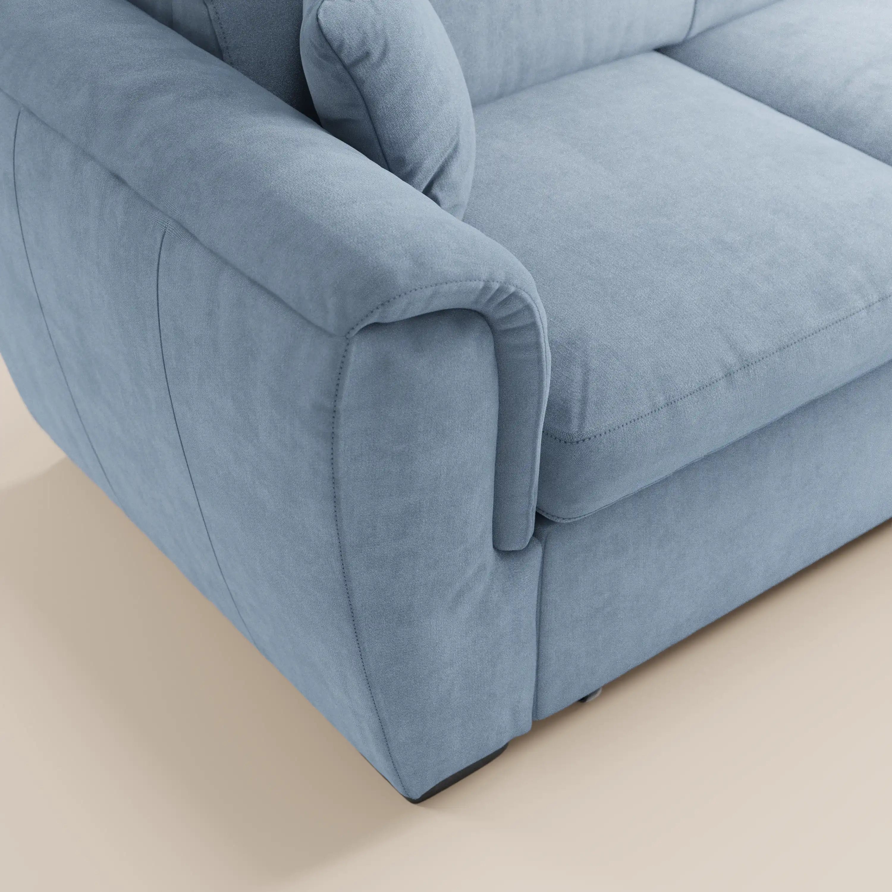 Primo piano del divano letto Titano con penisola reversibile di Divani.Store, rivestito in tessuto ant macchia azzurro chiaro con braccioli imbottiti, cuciture a vista e texture morbida. Sullo sfondo, pavimento beige chiaro.