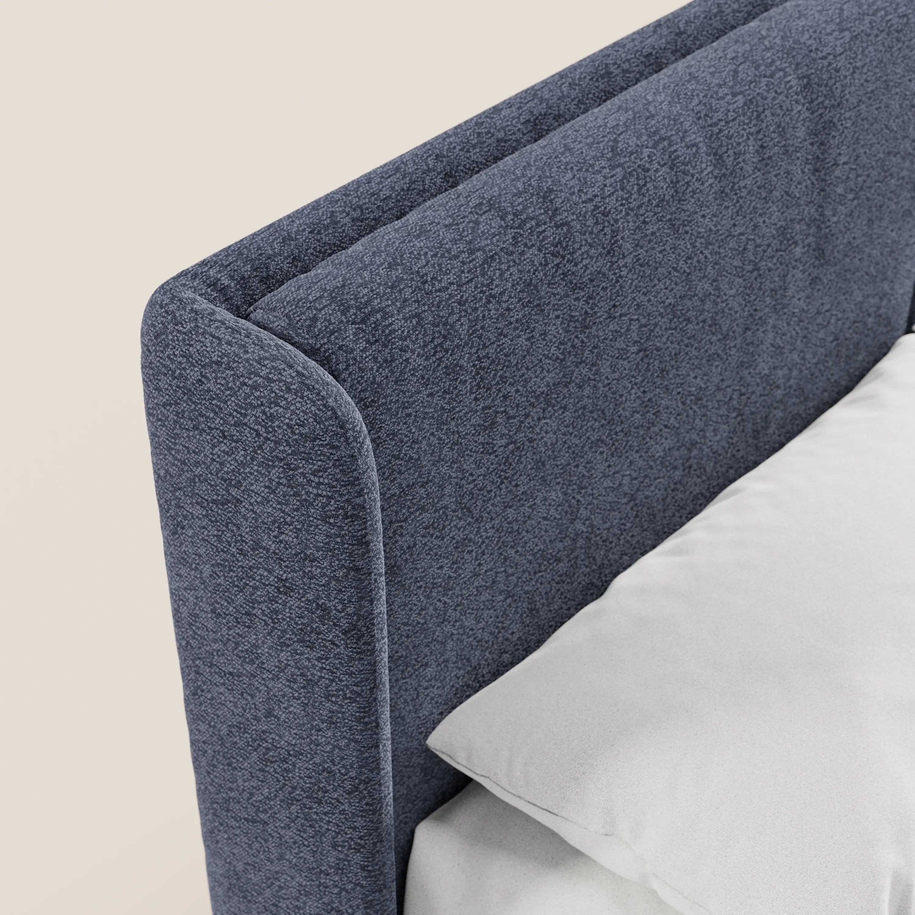 Primo piano del letto di design VALKIRIA di Letti.store, caratterizzato da una testiera in tessuto blu scuro certificato Oeko-Tex® con bordi arrotondati e avvolgenti e 2 morbidi cuscini. La sua linea moderna crea un contrasto con un cuscino bianco su uno sfondo neutro.