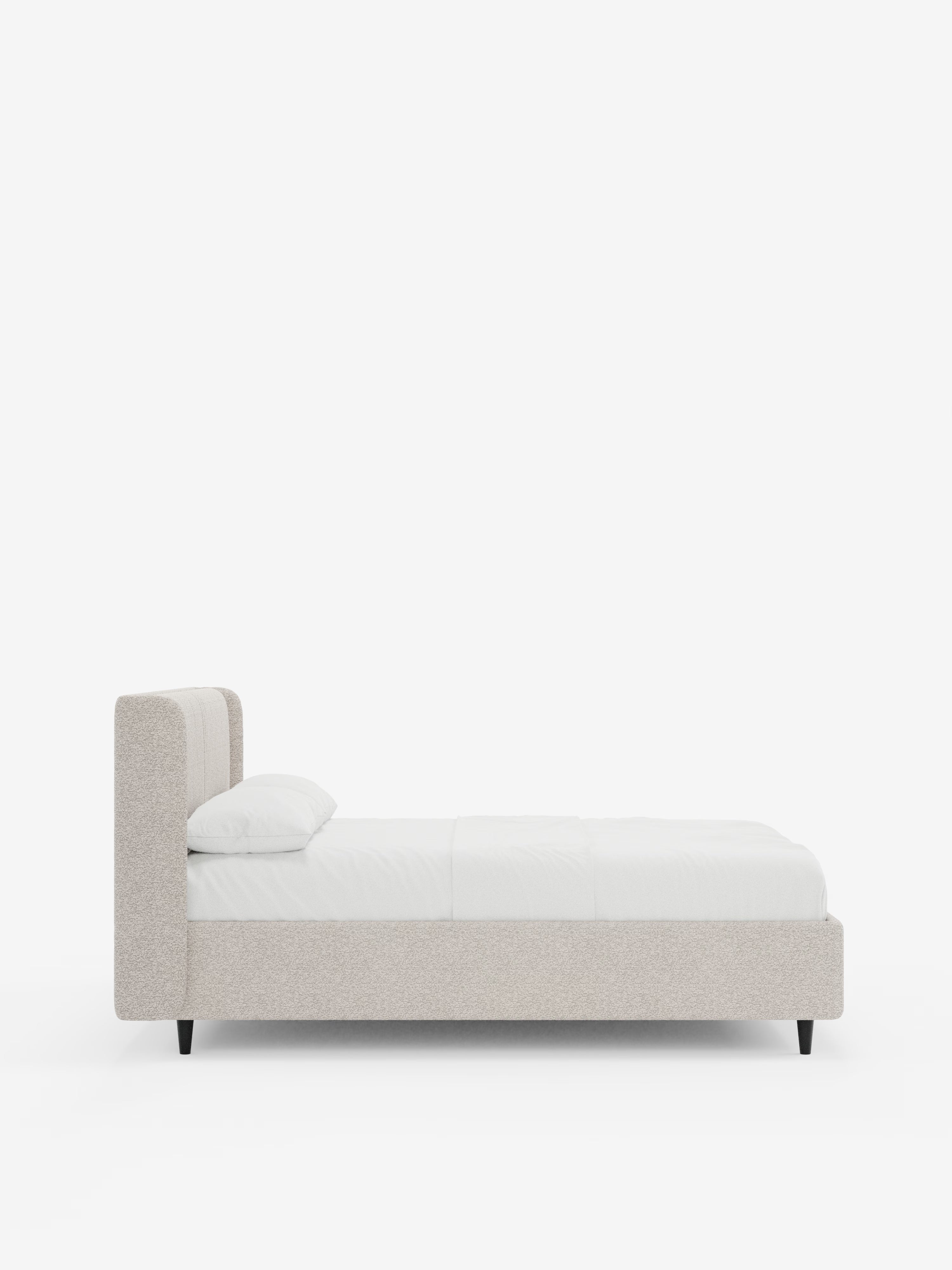 Una vista laterale del letto di design VALKIRIA di Letti.store, caratterizzato da una struttura imbottita (letto imbottito) in beige chiaro certificata Oeko-Tex® in stile contemporaneo. Presenta una testiera alta e avvolgente con due cuscini imbottiti, biancheria da letto bianca e un cuscino singolo. Il letto poggia su gambe nere corte e angolate su uno sfondo bianco a tinta unita e include un vano contenitore integrato. Totale caratteri: 347.