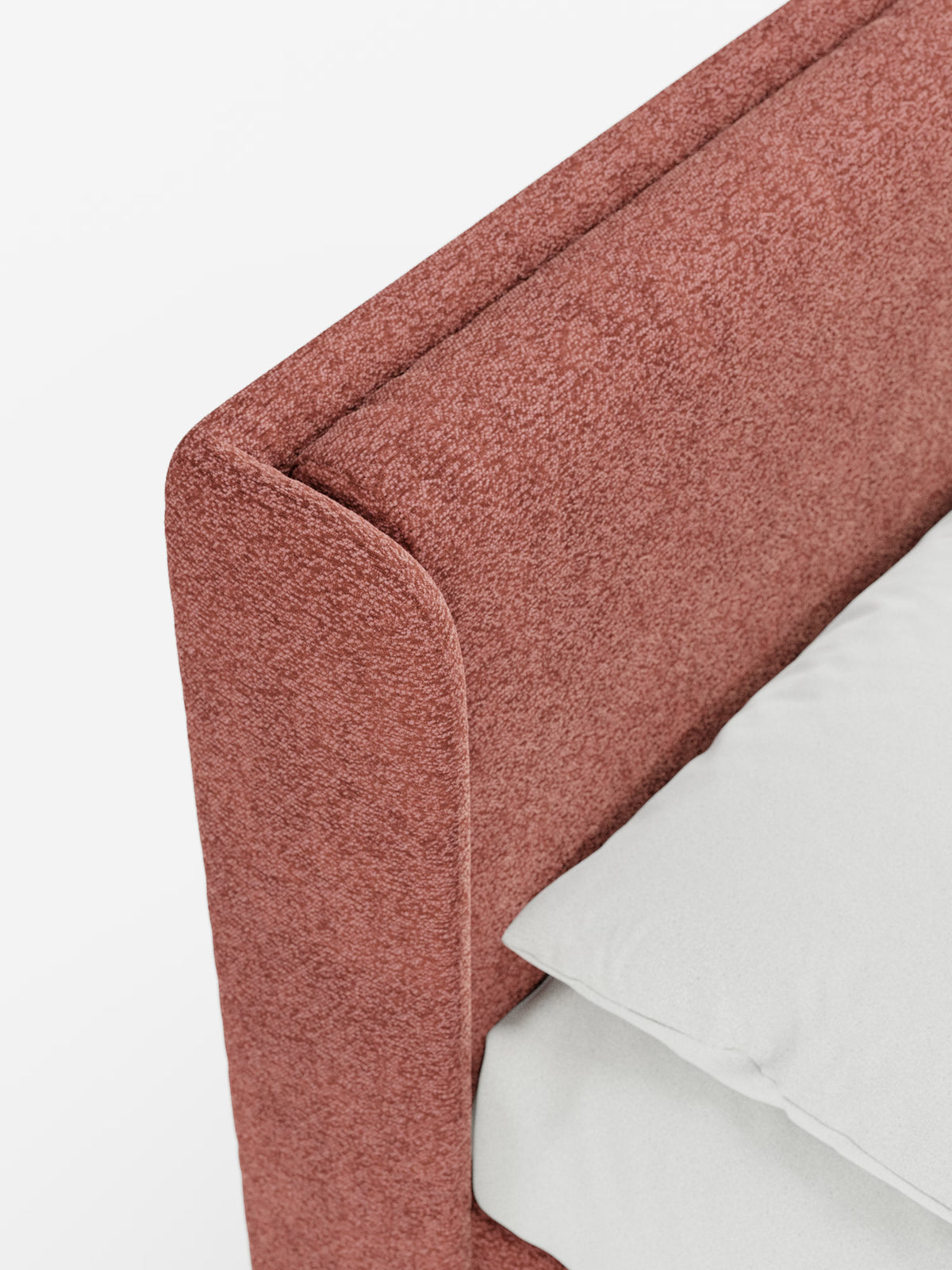 Primo piano di un angolo del letto che mette in risalto il “VALKIRIA”, letto di design con vano contenitore e testiera avvolgente di Letti.store, rivestito in morbido tessuto Oeko-Tex® rosso tenue dalla trama ricca. Due morbidi poggiatesta imbottiti accentuano l’eleganza della struttura. Un cuscino e un lenzuolo di un bianco immacolato sono disposti con cura sul materasso, mentre lo sfondo bianco a tinta unita mette in risalto il design contemporaneo e i lussuosi dettagli del tessuto di questo raffinato
