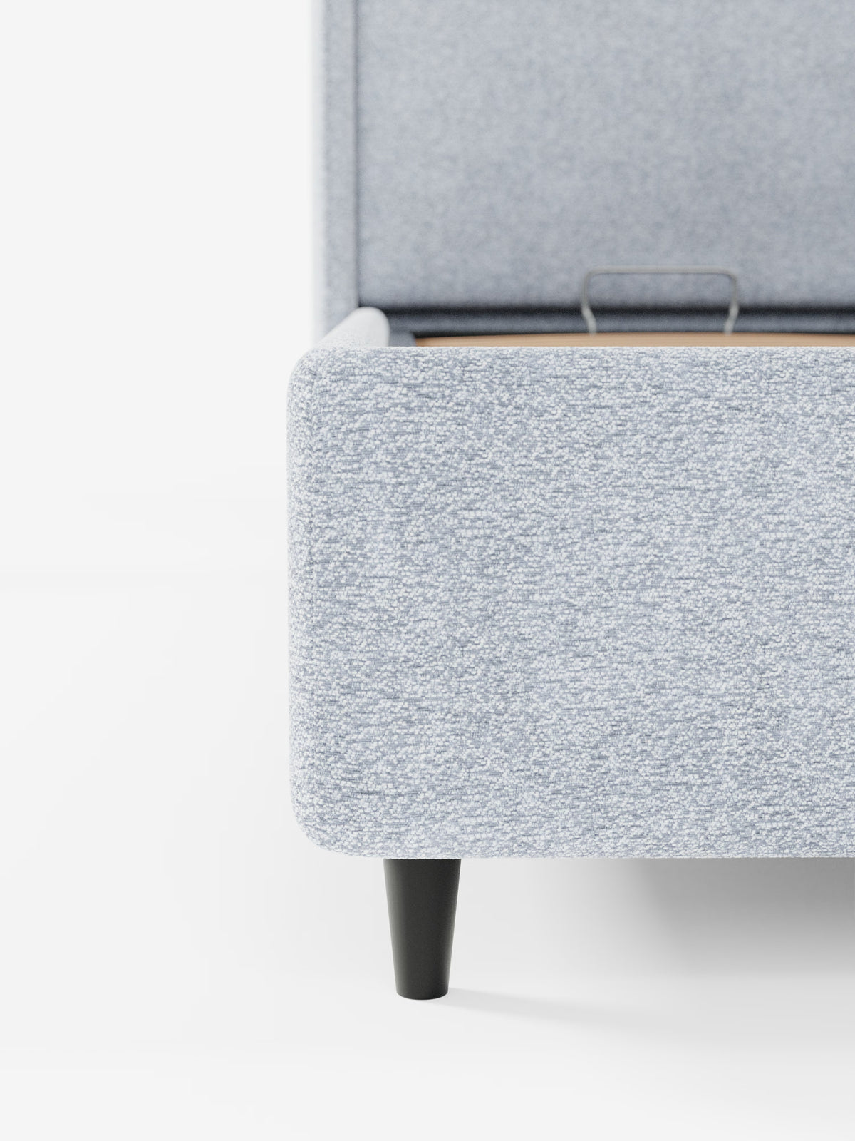 Primo piano dell'angolo di VALKIRIA, il letto di design di Letti.store, rivestito in tessuto Oeko-Tex® grigio chiaro. La finitura testurizzata, le doghe in legno a vista e l'unica gamba affusolata nera ne esaltano lo stile contemporaneo. Il look è minimalista e pulito sullo sfondo bianco, con una parte della testiera avvolgente e uno dei due cuscini imbottiti appena visibili dietro la struttura.