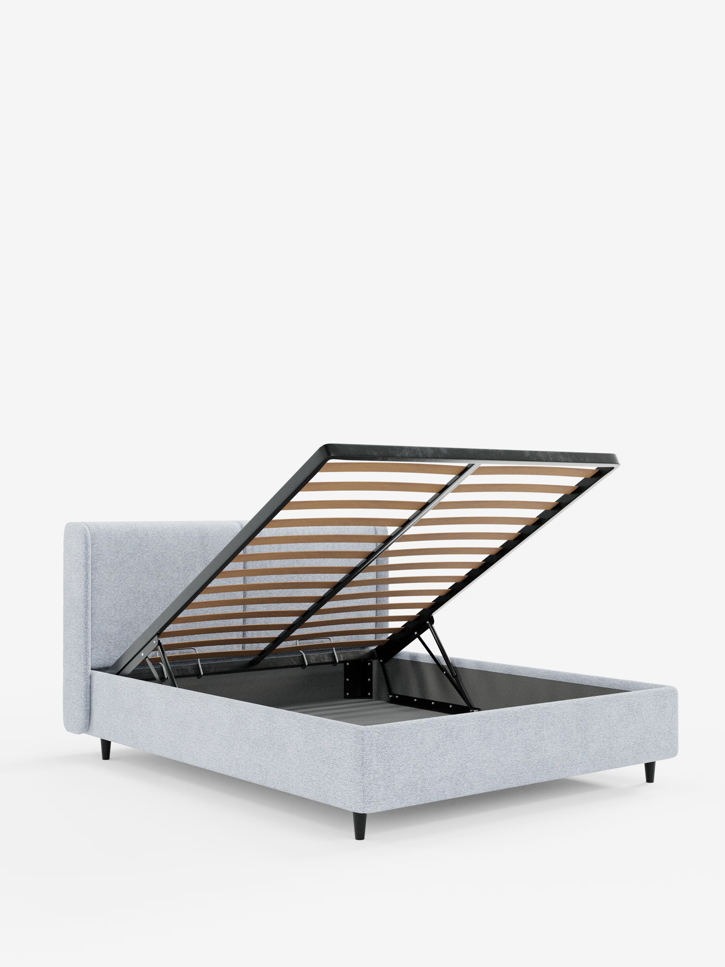 Il letto di design VALKIRIA con vano contenitore e testiera avvolgente di Letti.store presenta una struttura imbottita grigio chiaro con gambe nere. La rete a doghe è raffigurata sollevata, rivelando un ampio spazio di stoccaggio sotto il letto. Su uno sfondo bianco a tinta unita, il letto mette in risalto il suo design contemporaneo e la pratica funzionalità di contenimento, esaltata da due cuscini imbottiti e dal tessuto certificato Oeko-Tex®.