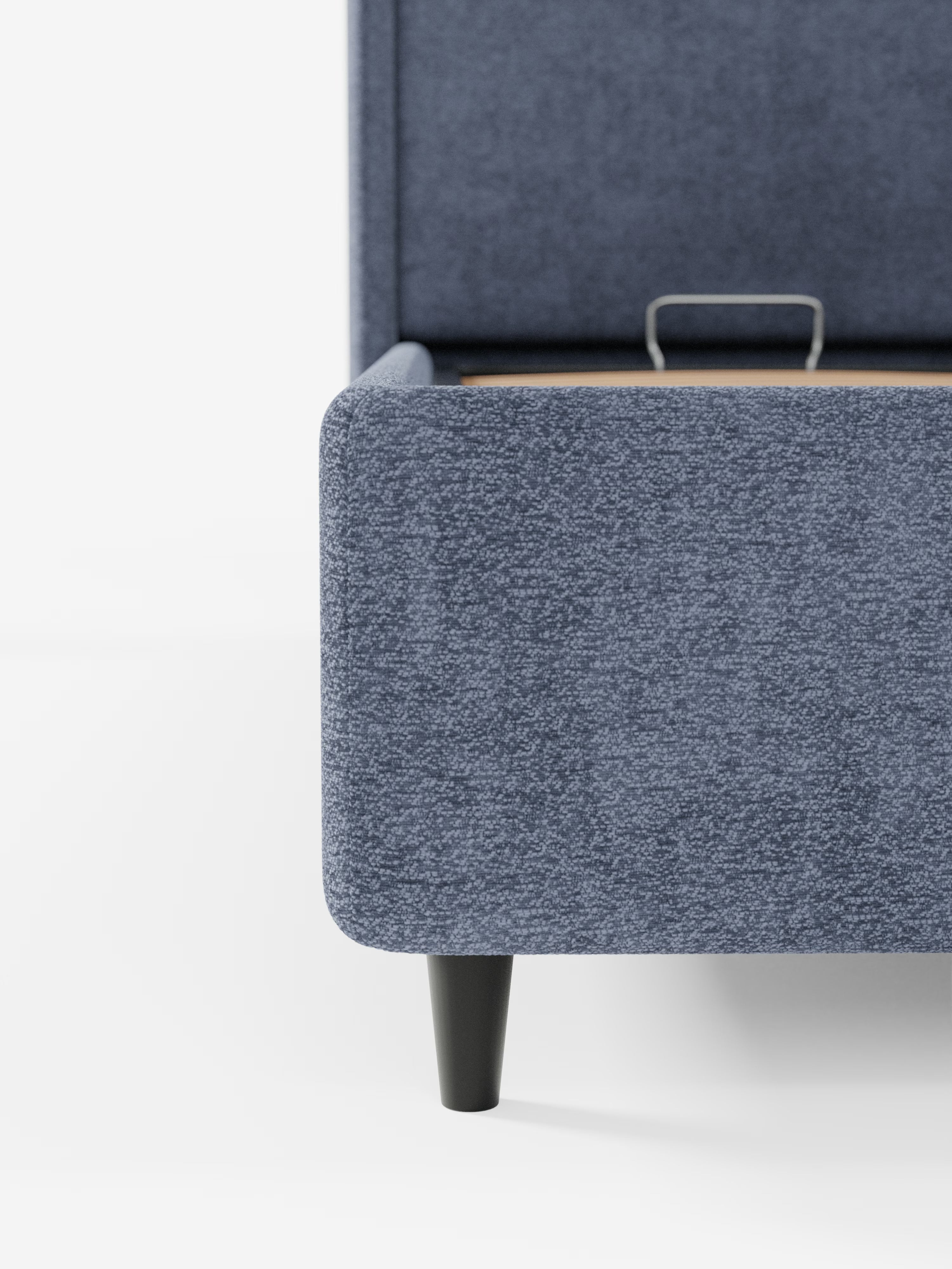 Primo piano dell'angolo del letto di design VALKIRIA con vano contenitore e testiera avvolgente di Letti.store, rivestito in tessuto blu testurizzato certificato Oeko-Tex®. Il design presenta un bordo arrotondato, gambe cilindriche nere e una piccola maniglia metallica sulla base del letto. Sullo sfondo bianco a tinta unita, risalta l’estetica contemporanea del letto con i suoi 2 cuscini imbottiti.