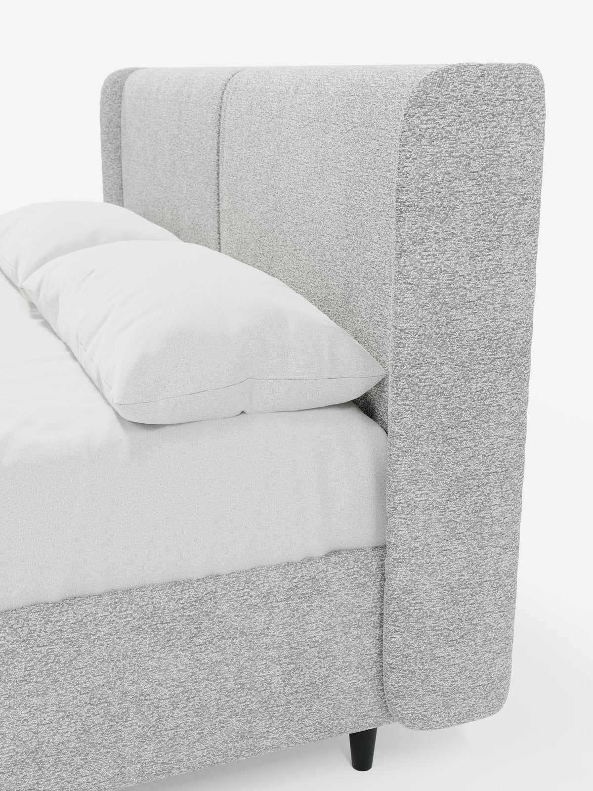 Un primo piano del letto di design VALKIRIA con vano contenitore e testiera avvolgente di Letti.store mette in risalto la sua testiera alta, rivestita in grigio chiaro con bordi arrotondati e due cuscini imbottiti, che ne sottolineano il design contemporaneo. Il letto imbottito è caratterizzato da biancheria da letto e cuscini bianchi adagiati su una base robusta con gambe corte nere, il tutto su uno sfondo bianco a tinta unita. Rivestito in tessuto certificato Oeko-Tex®, il letto coniuga perfettamente