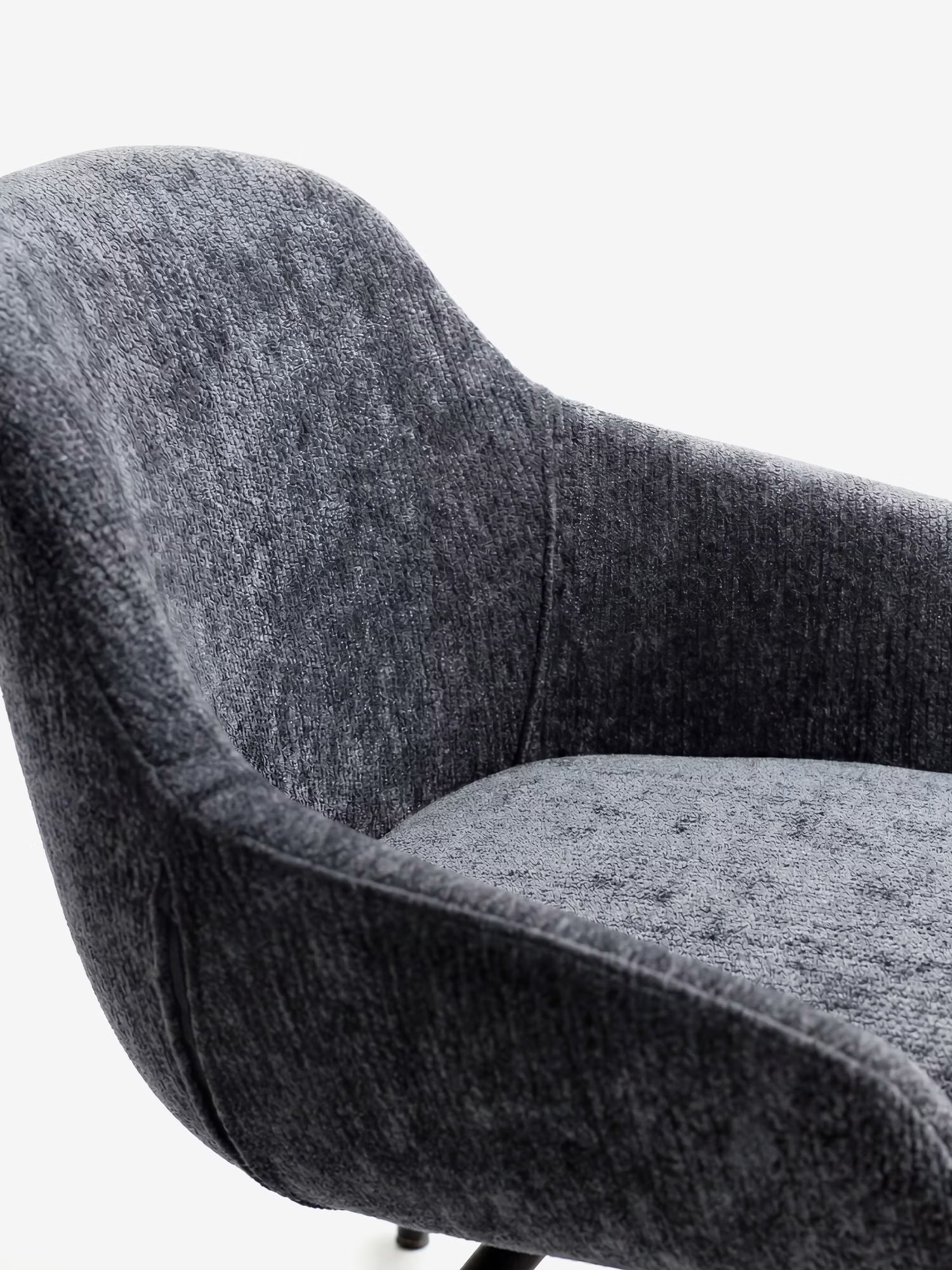 Primo piano della sedia imbottita Vico di Divani.Store, realizzata in morbido tessuto grigio scuro certificato OEKO-TEX® e dotata di gambe in metallo nero. Le sue linee slanciate e arrotondate e lo schienale curvo creano un look accogliente e contemporaneo sullo sfondo bianco.