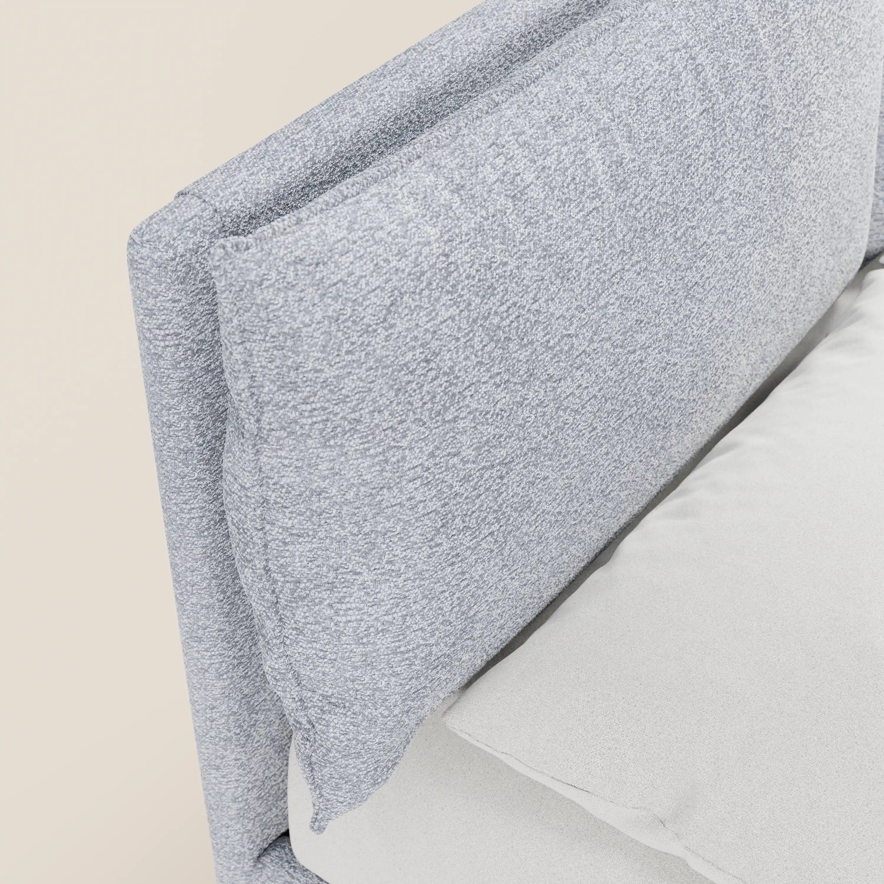 Primo piano del letto imbottito ZAYRON di Letti.store: la sua testiera regolabile e morbida, realizzata in tessuto grigio chiaro certificato Oeko-Tex®, è abbinata a cuscini coordinati e a un materasso bianco, il tutto su uno sfondo bianco sporco.