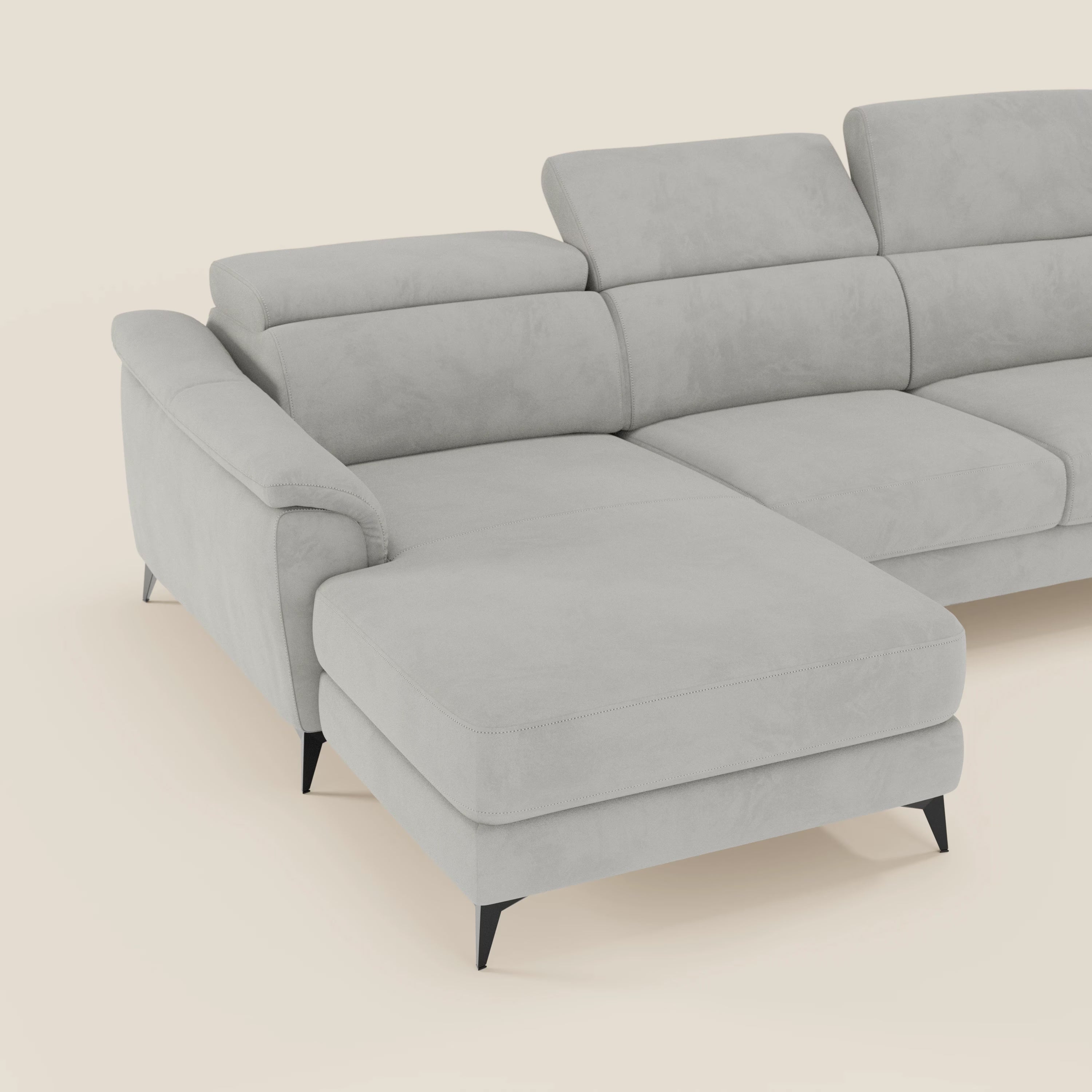 L'Arcos Divano con penisola di Divani.Store, in microfibra grigia chiara T11, con piedini alti e poggiatesta reclinabili, esemplifica la manifattura italiana su un semplice sfondo crema.