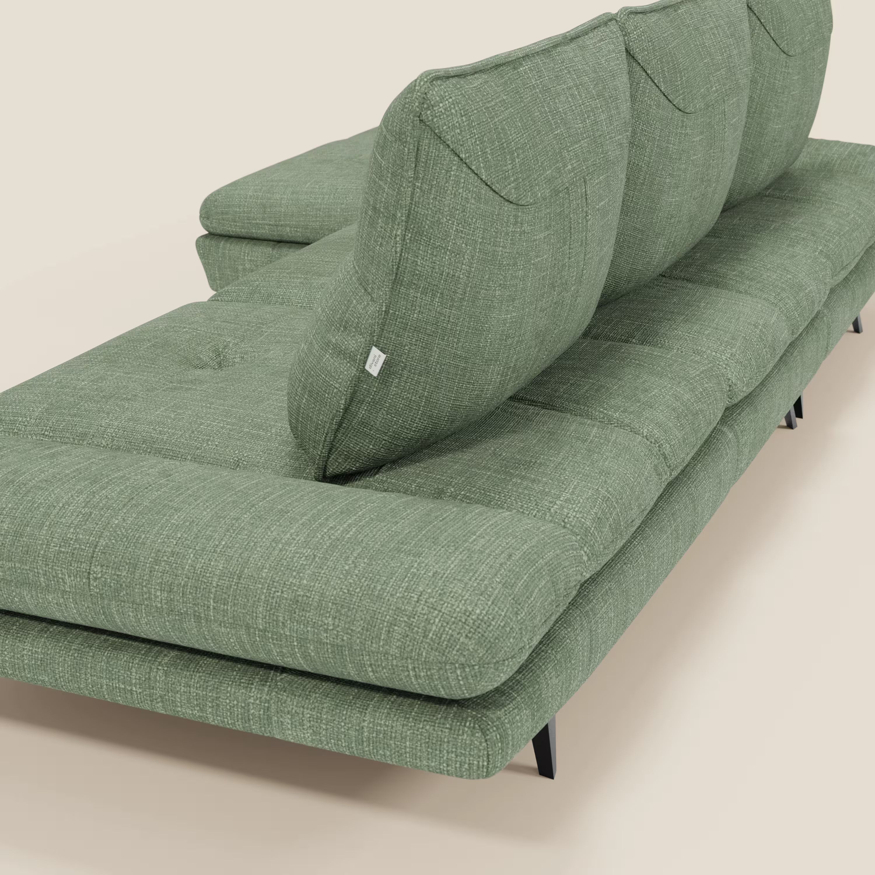 Ardex Divano con penisola di Divani.Store, in elegante tessuto impermeabile verde T06, è dotato di schienale scorrevole, braccioli regolabili e sottili gambe in metallo nero. In figura, di lato e con lo schienale su sfondo beige chiaro.