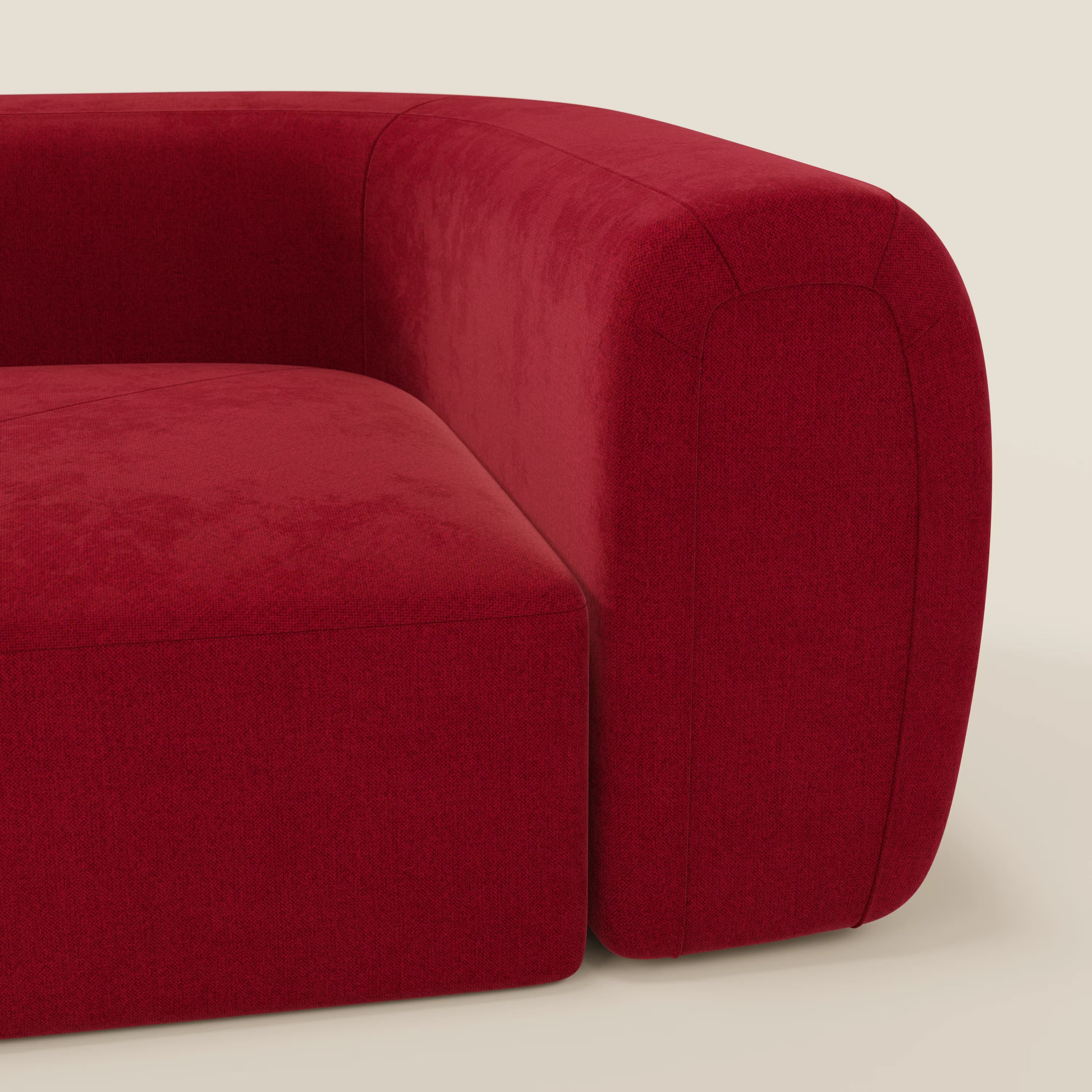 Un primo piano di Bonbon Modulo angolare di Divani.Store, un moderno divano modulare in tessuto antimacchia T23 bordeaux, mette in evidenza il bracciolo e la seduta lisci e arrotondati su uno sfondo beige chiaro. Il rivestimento appare morbido e dalle linee pulite.