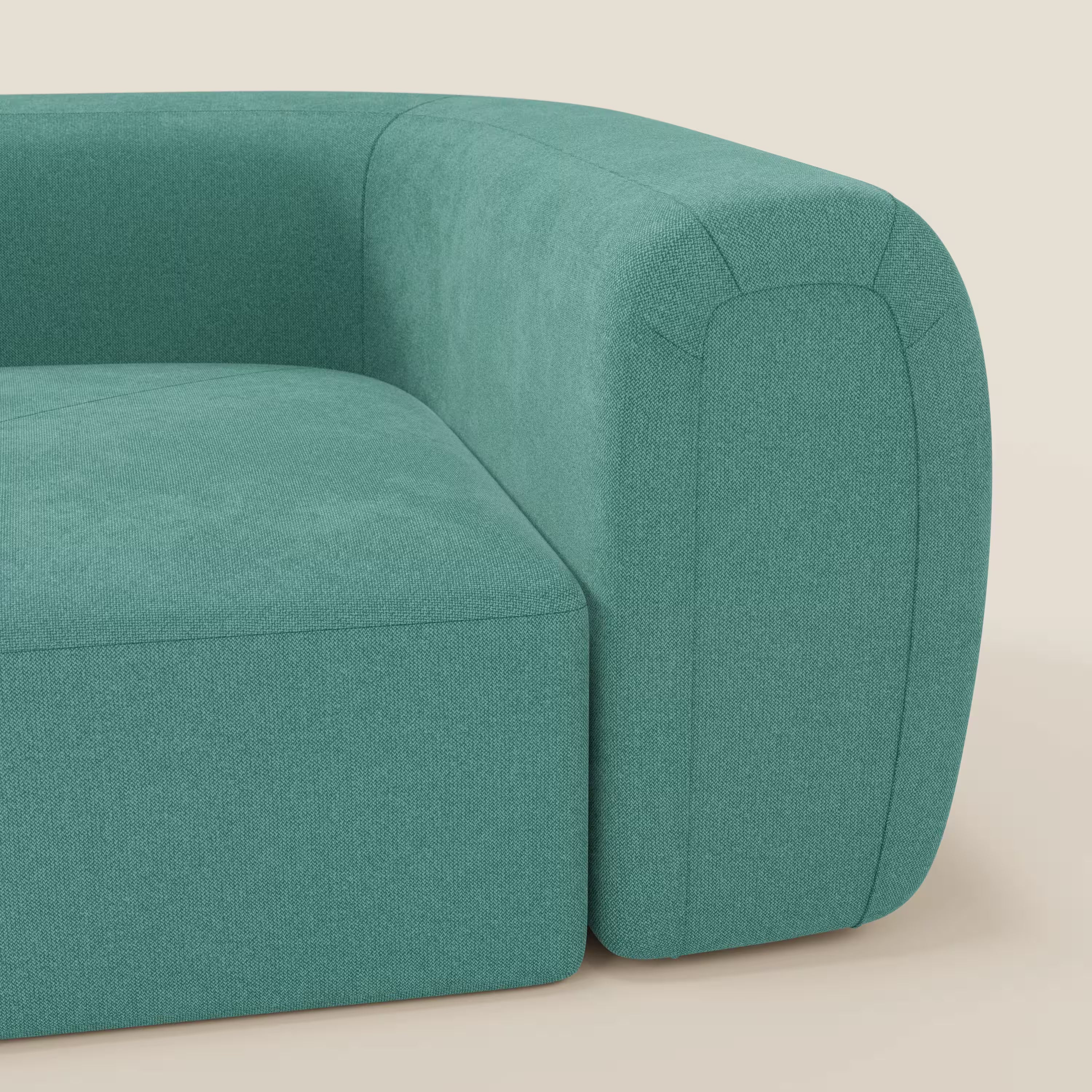 Primo piano del bracciolo sinistro e della seduta di Bonbon Modulo angolare di Divani.Store, un moderno divano componibile in tessuto T23 antimacchia verde acqua, con bordi puliti e arrotondati e cuciture minimaliste, su uno sfondo beige chiaro.