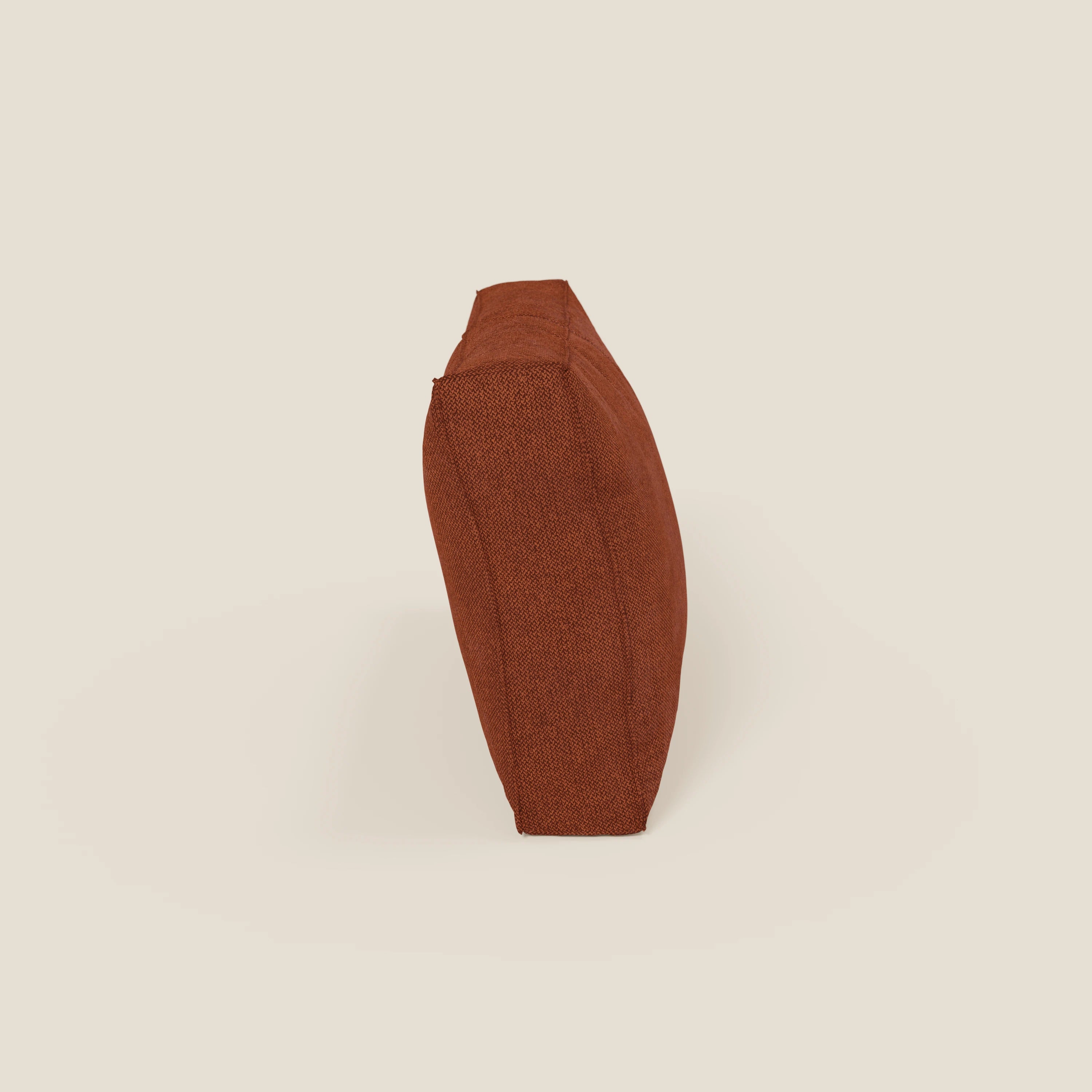 Un cuscino schienale quadrato BonBon di Divani.Store in tessuto smacchiabile T23 si erge sul bordo su uno sfondo beige chiaro, sottolineando il suo profilo sottile e il colore rosso mattone. Disponibile in 2 misure.