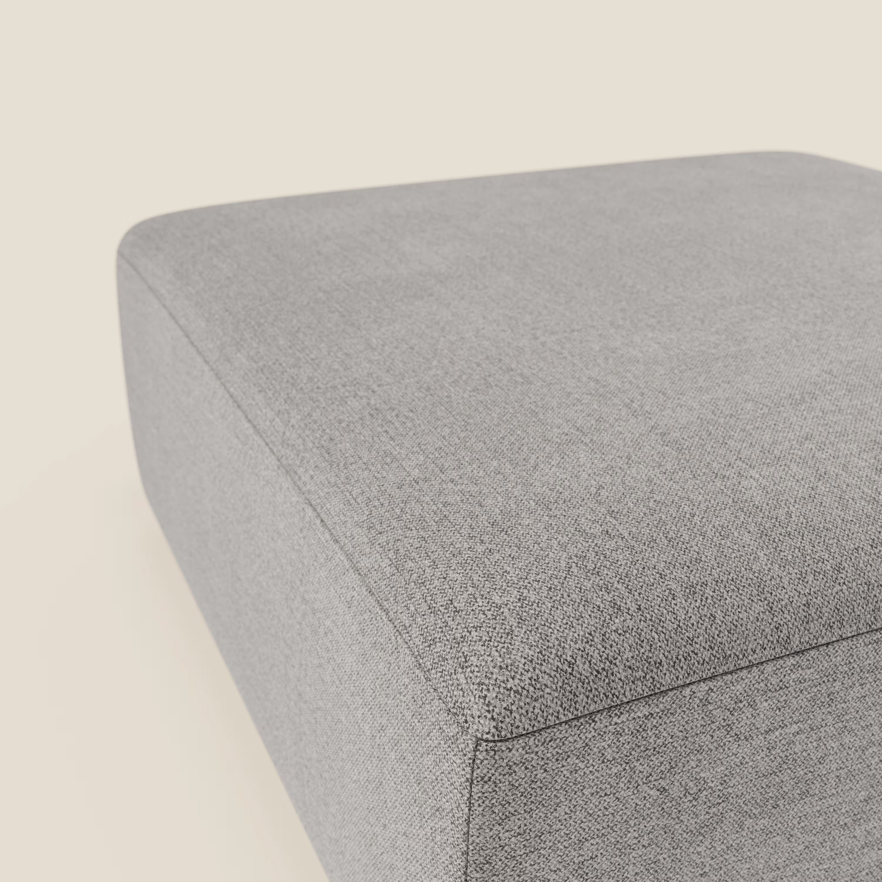 Un primo piano del pouf divano modulare BonBon di Divani.Store in tessuto antimacchia T23 grigio chiaro. Il suo design elegante e rettangolare e la sua texture liscia spiccano su uno sfondo bianco sporco.