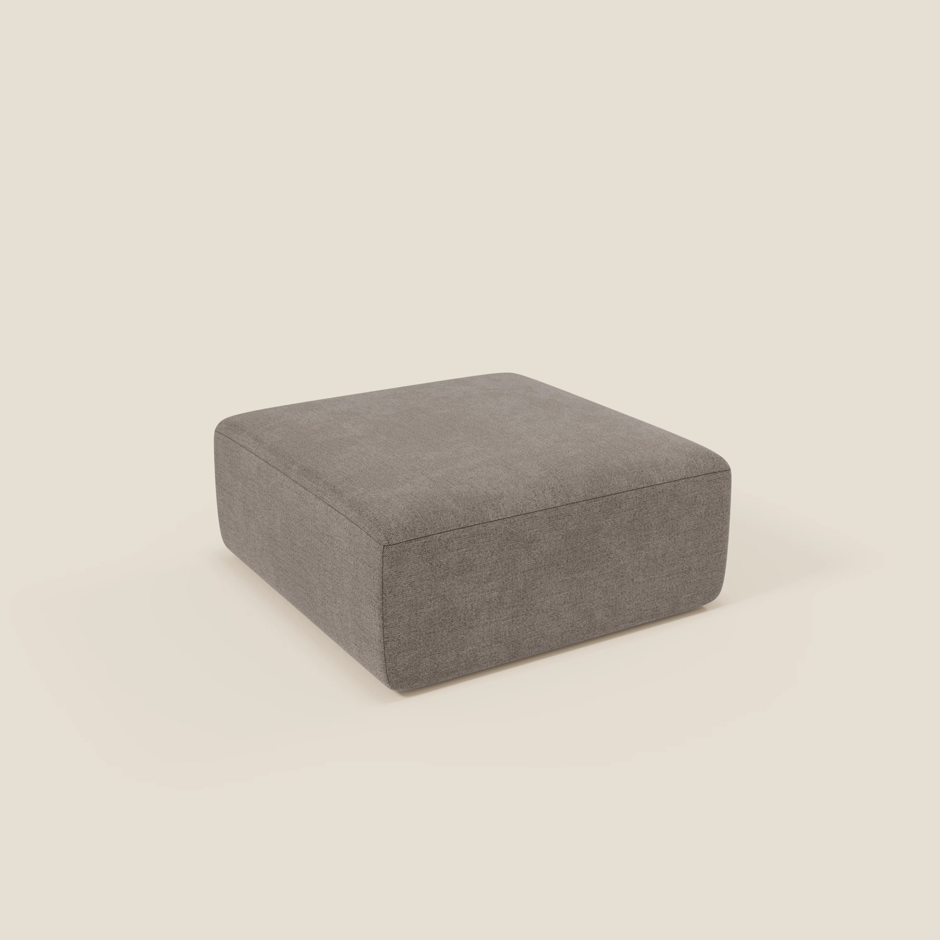 Il pouf divano modulare BonBon di Divani.Store in tessuto smacchiabile T23 talpa presenta un design grigio e squadrato con imbottitura liscia, bordi puliti e un profilo basso per un look elegante e moderno. Mostrato su uno sfondo beige chiaro.