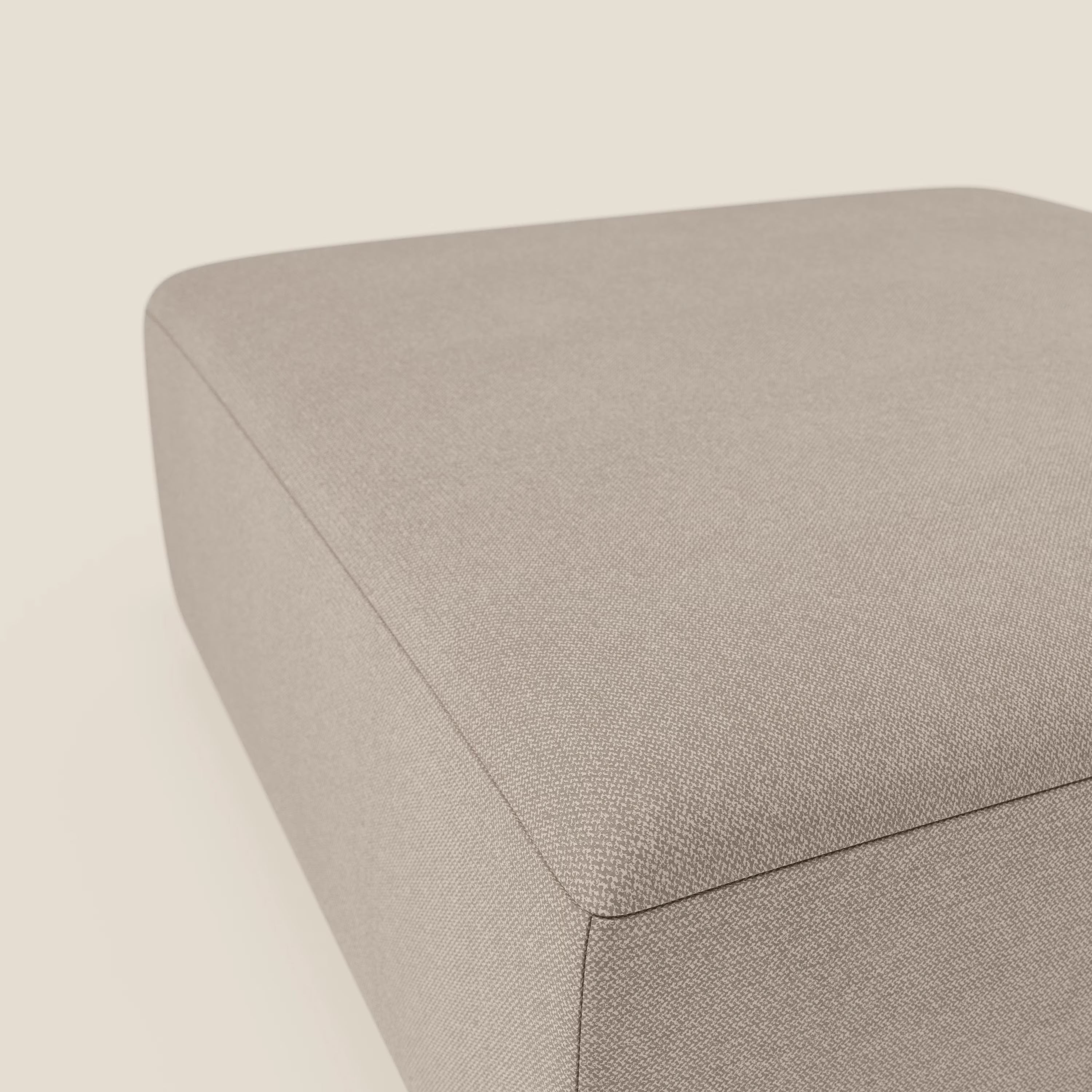 Un primo piano del pouf divano modulare BonBon di Divani.Store in tessuto tortora antimacchia T23 mostra il suo design rettangolare dai bordi morbidi su uno sfondo crema chiaro, evidenziandone il fascino minimalista e moderno.