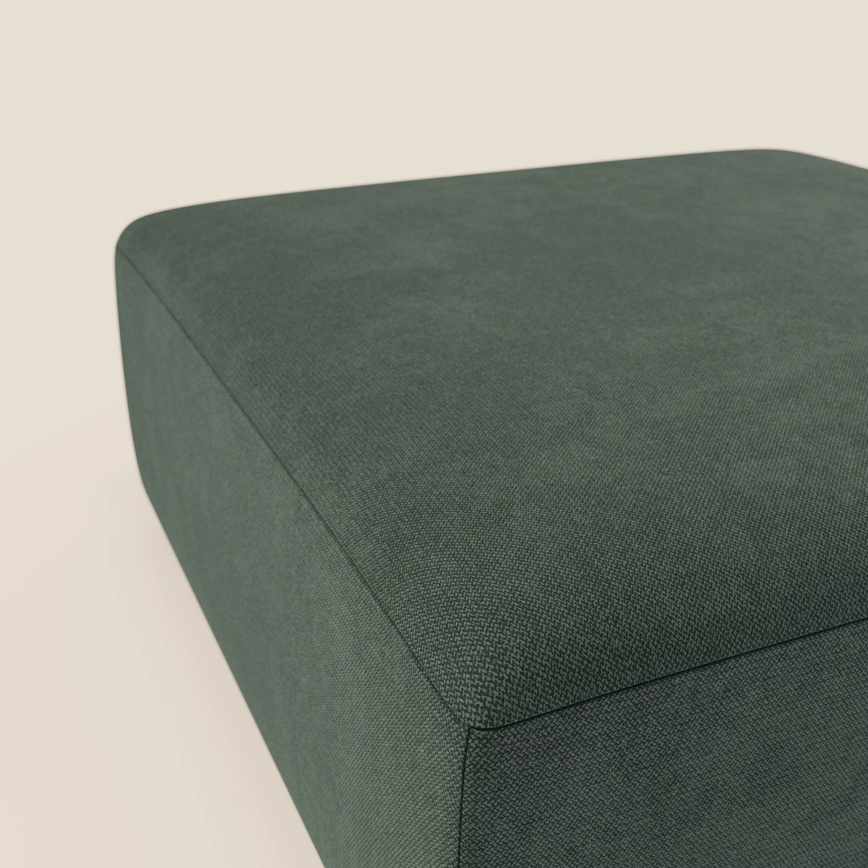 Primo piano del pouf divano modulare BonBon di Divani.Store, presentato in tessuto antimacchia verde T23. Il pouf quadrato è appoggiato su uno sfondo beige chiaro, con solo la parte superiore e i lati visibili per un look moderno.