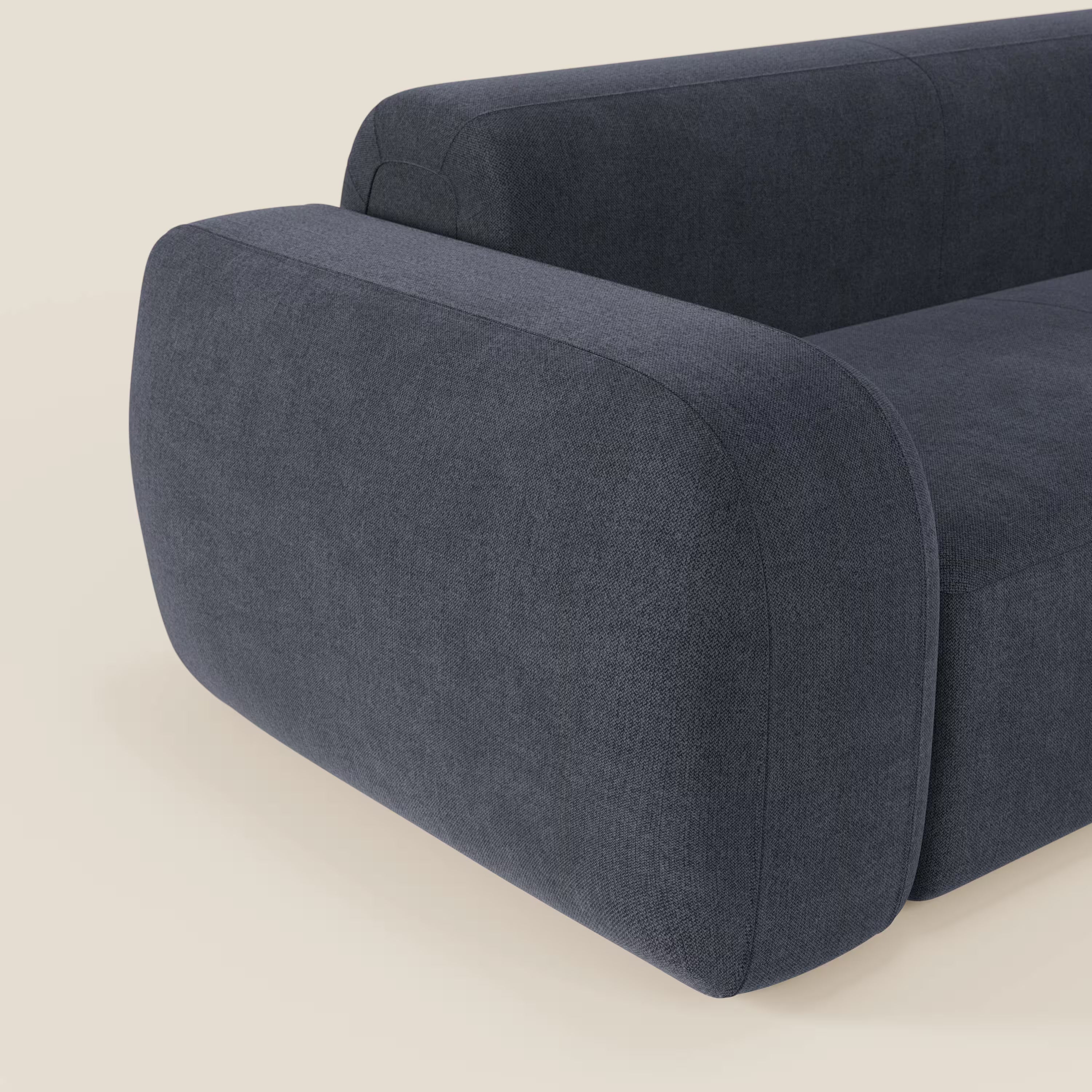 Un primo piano del BonBon Divano modulare Lineare 220 di Divani.Store, rivestito in smacchiabile ardesia T23 blu, mostra il bracciolo spesso e arrotondato e il design elegante e minimalista su un semplice sfondo bianco sporco.