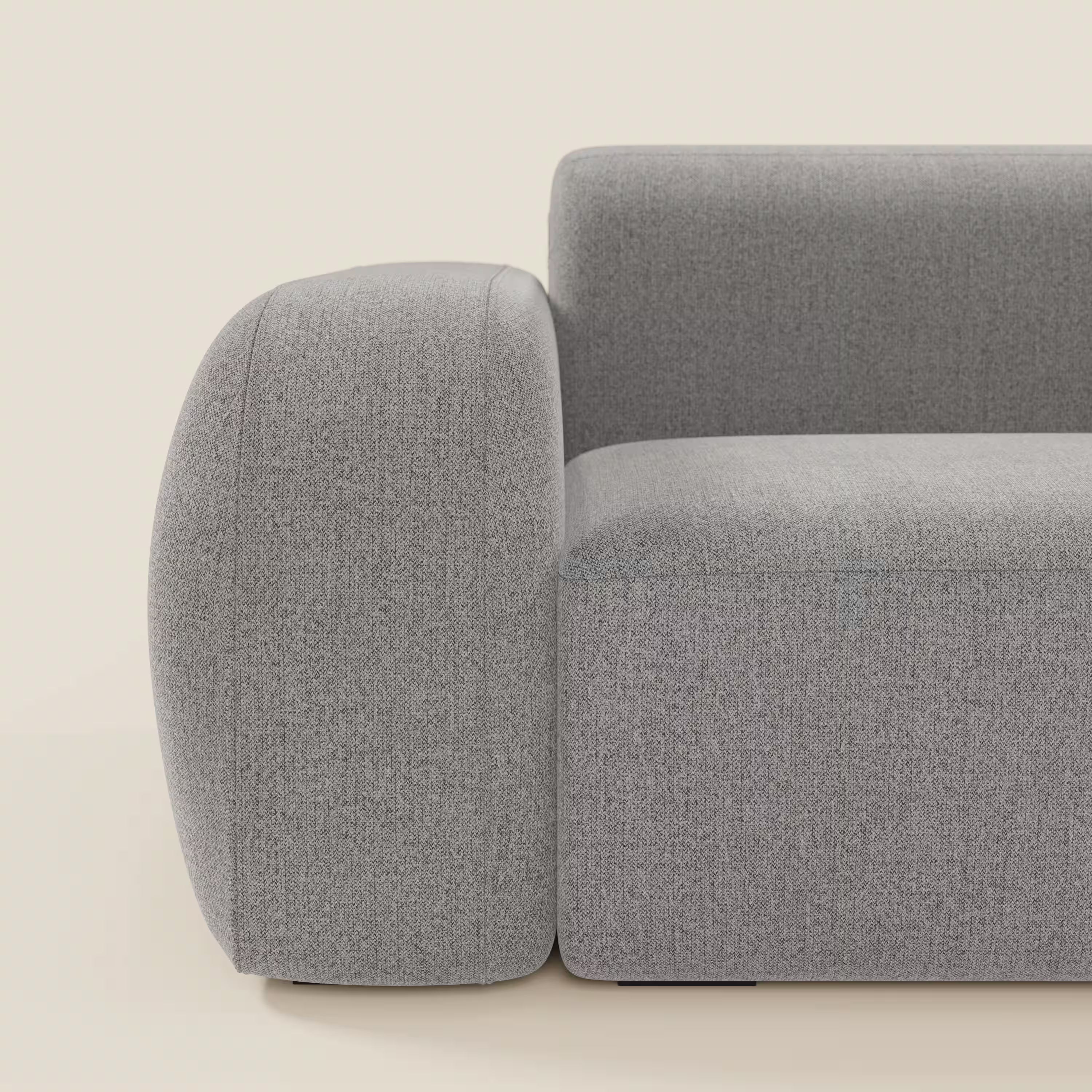 Una vista laterale ravvicinata del BonBon Divano modulare Lineare 220 di Divani.Store mostra braccioli e schienale spessi e arrotondati in tessuto liscio e antimacchia grigio T23, con linee pulite e un'unica seduta, su uno sfondo beige chiaro.