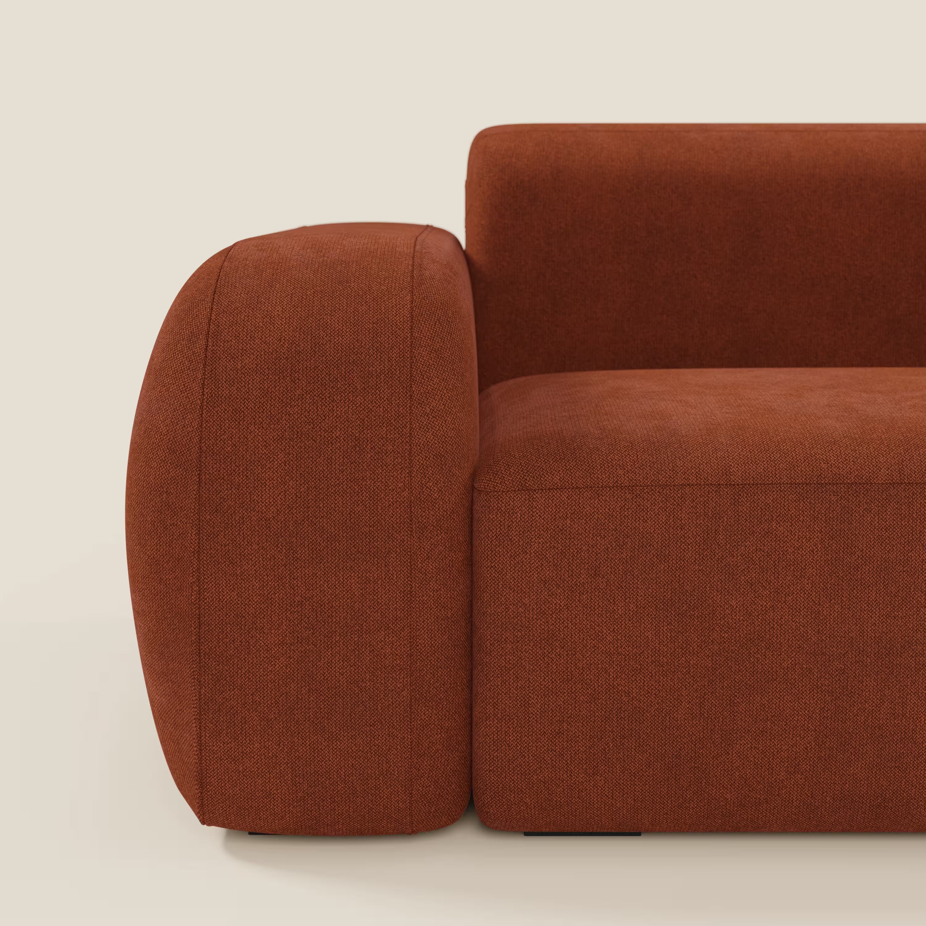 Primo piano del BonBon Divano modulare Lineare 220 con seduta unica in tessuto smacchiabile T23 ruggine di Divani.Store, che mostra il bracciolo sinistro spesso e arrotondato e la seduta su uno sfondo minimalista bianco sporco.