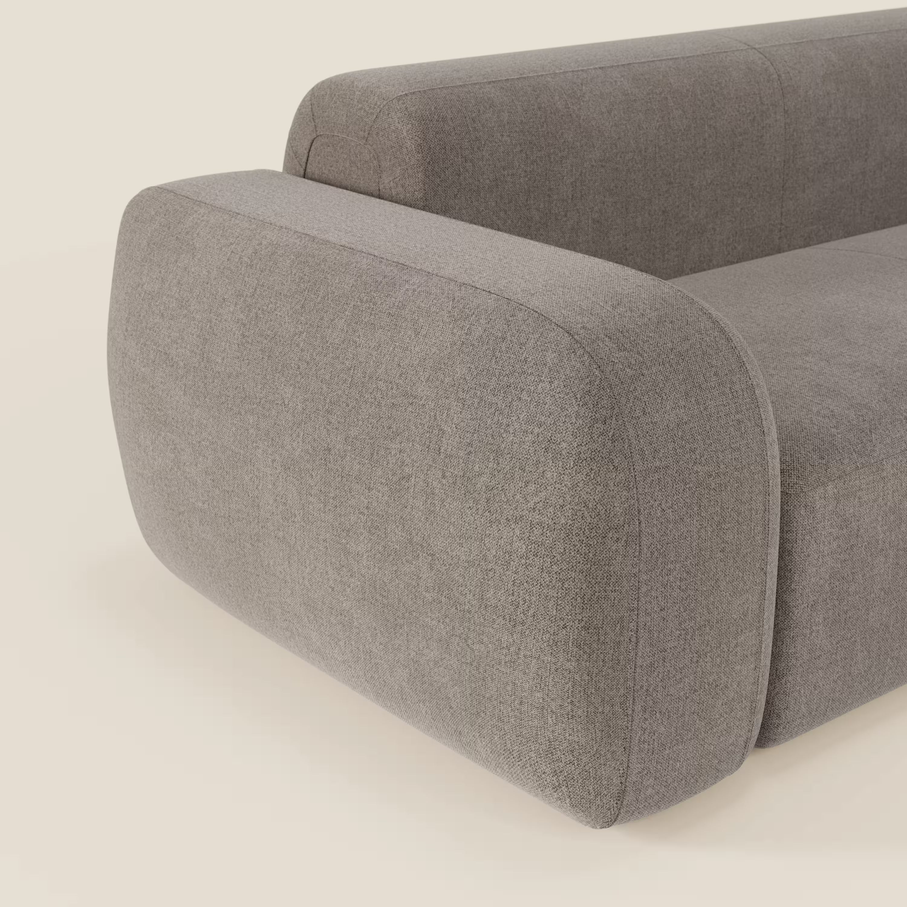 Primo piano del BonBon Divano modulare Lineare 220 di Divani.Store, caratterizzato da braccioli e schienale arrotondati in tessuto talpa smacchiabile T23, su uno sfondo bianco sporco. Viene mostrata solo una parte del divano.