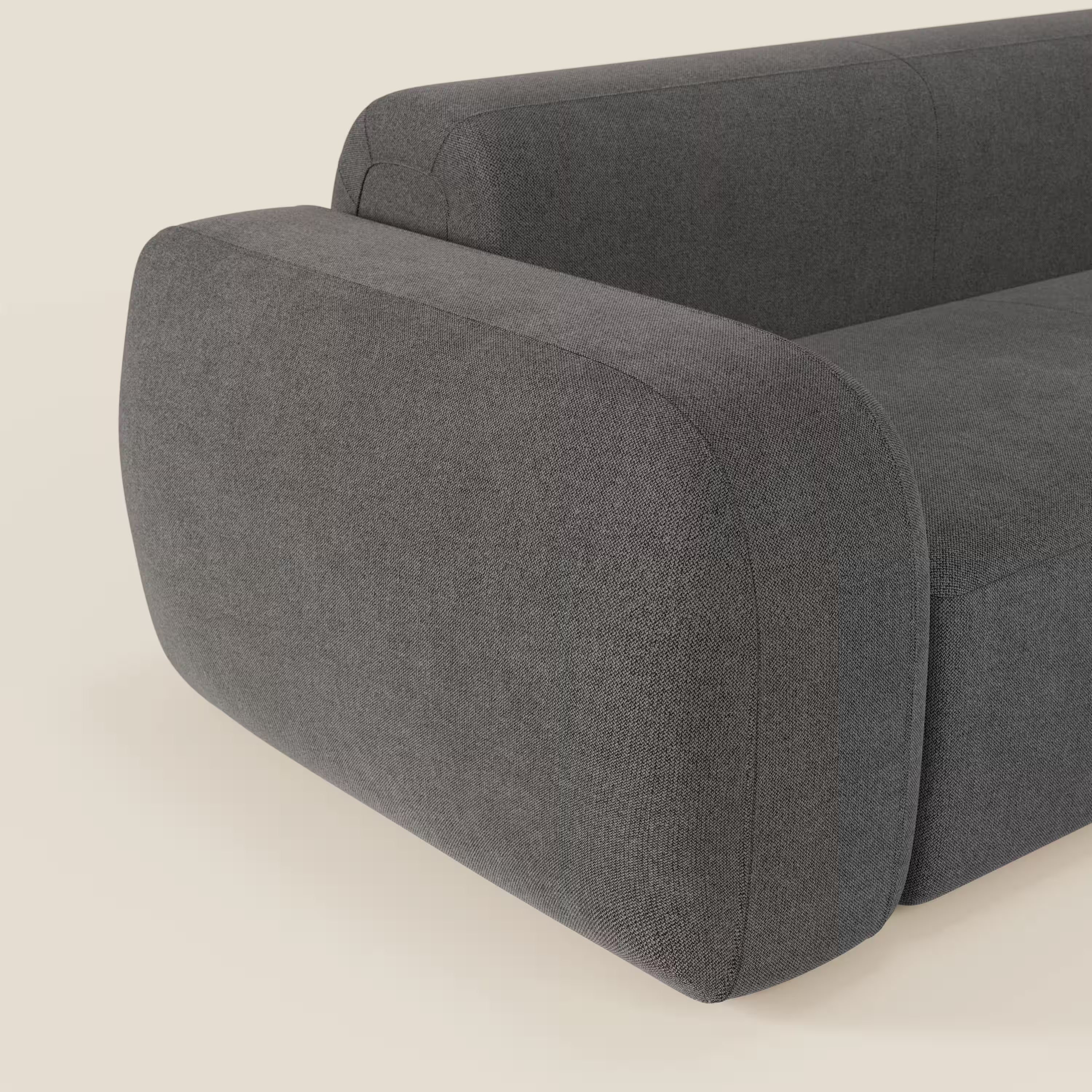 Un primo piano del divano componibile BonBon Divano di Divani.Store, in tessuto antracite T23 antimacchia con pouf terminale, evidenzia gli spessi braccioli arrotondati e il look minimalista su uno sfondo beige chiaro.