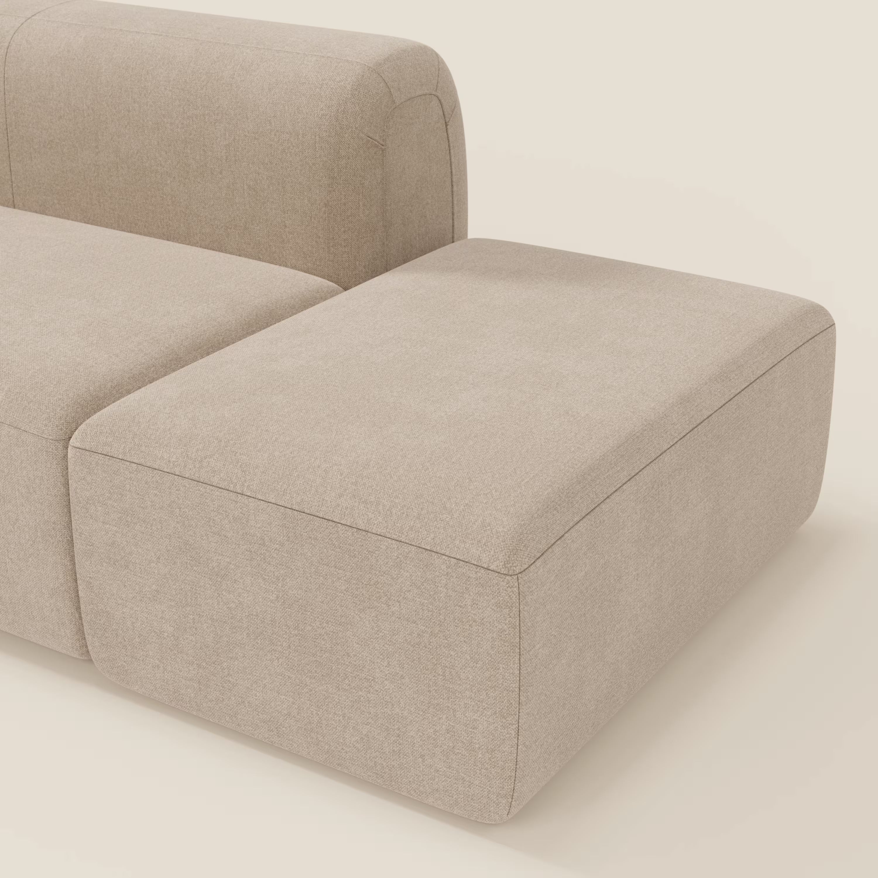 Primo piano del divano componibile BonBon Divano di Divani.Store in tessuto smacchiabile T23 beige, caratterizzato da un pouf terminale e da un design minimalista con linee pulite e bordi arrotondati, presentato su uno sfondo crema chiaro.