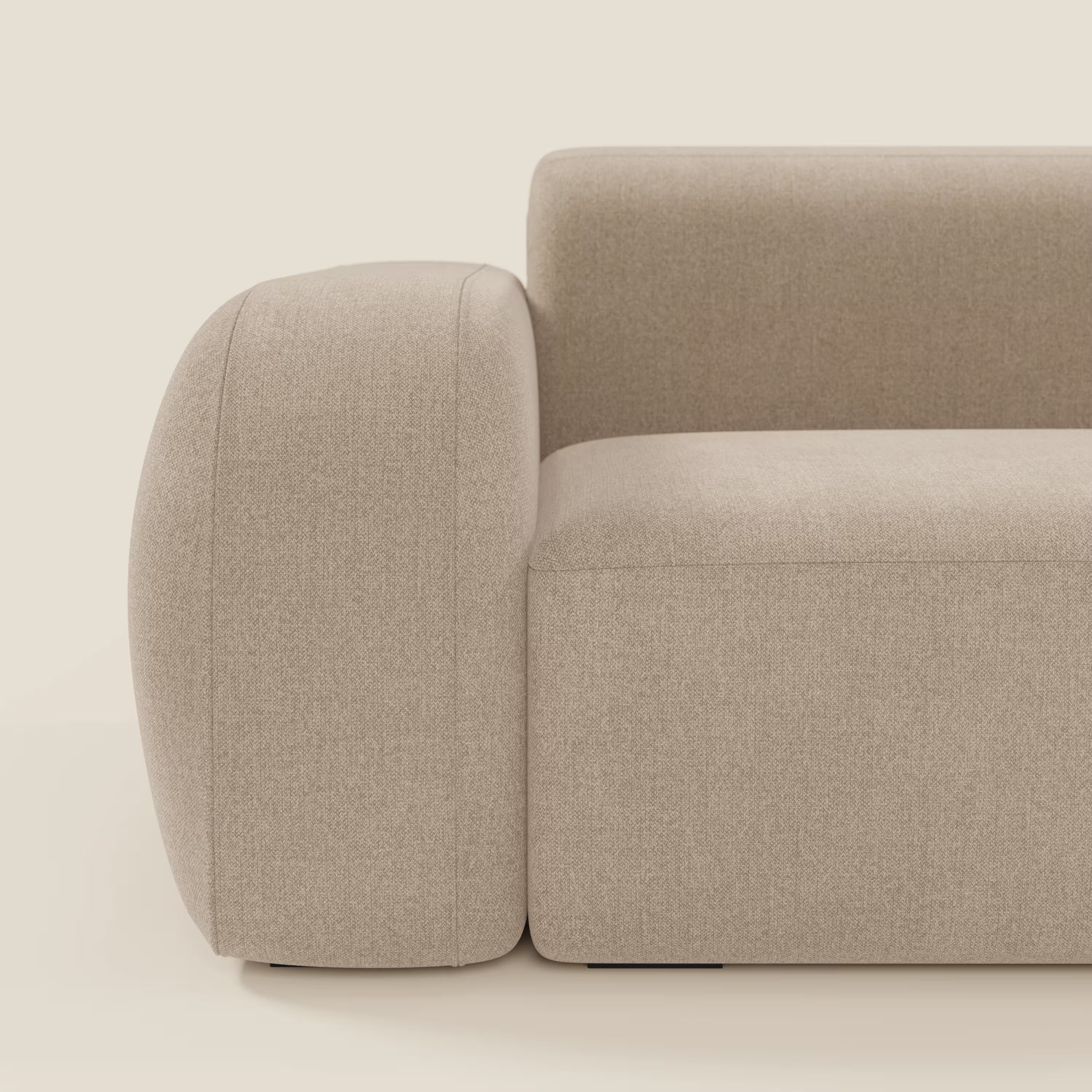 Vista laterale ravvicinata di BonBon Divano componibile di Divani.Store in smacchiabile T23 beige, caratterizzato da un bracciolo spesso e arrotondato e da un design minimalista. Il tessuto strutturato contrasta splendidamente con il fondo bianco sporco.