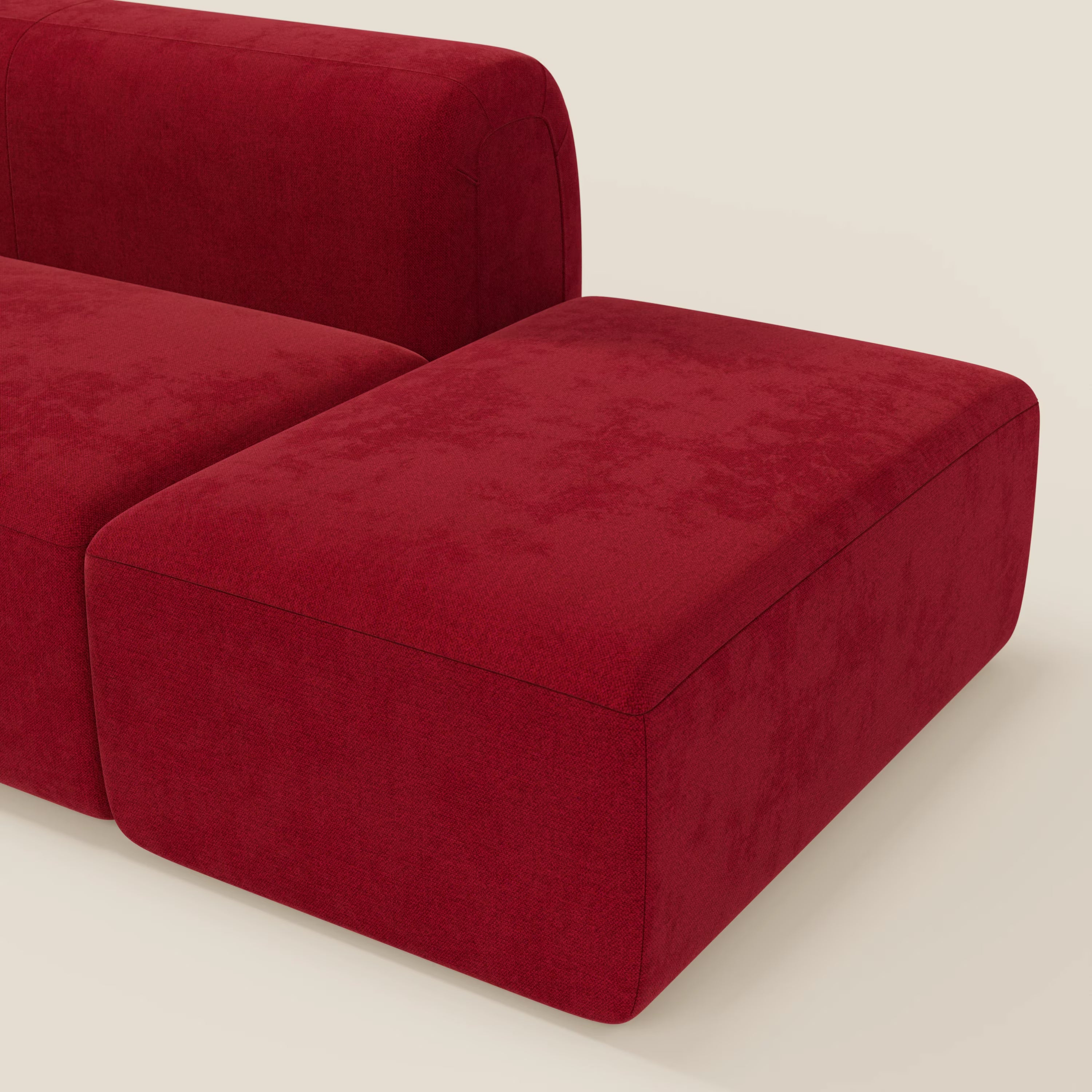 Il divano componibile BonBon Divano di Divani.Store, presentato in tessuto smacchiabile T23 bordeaux, è caratterizzato da cuscini in feltro e da un bracciolo angolare su uno sfondo beige chiaro; è visibile solo una parte del divano con pouf terminale.
