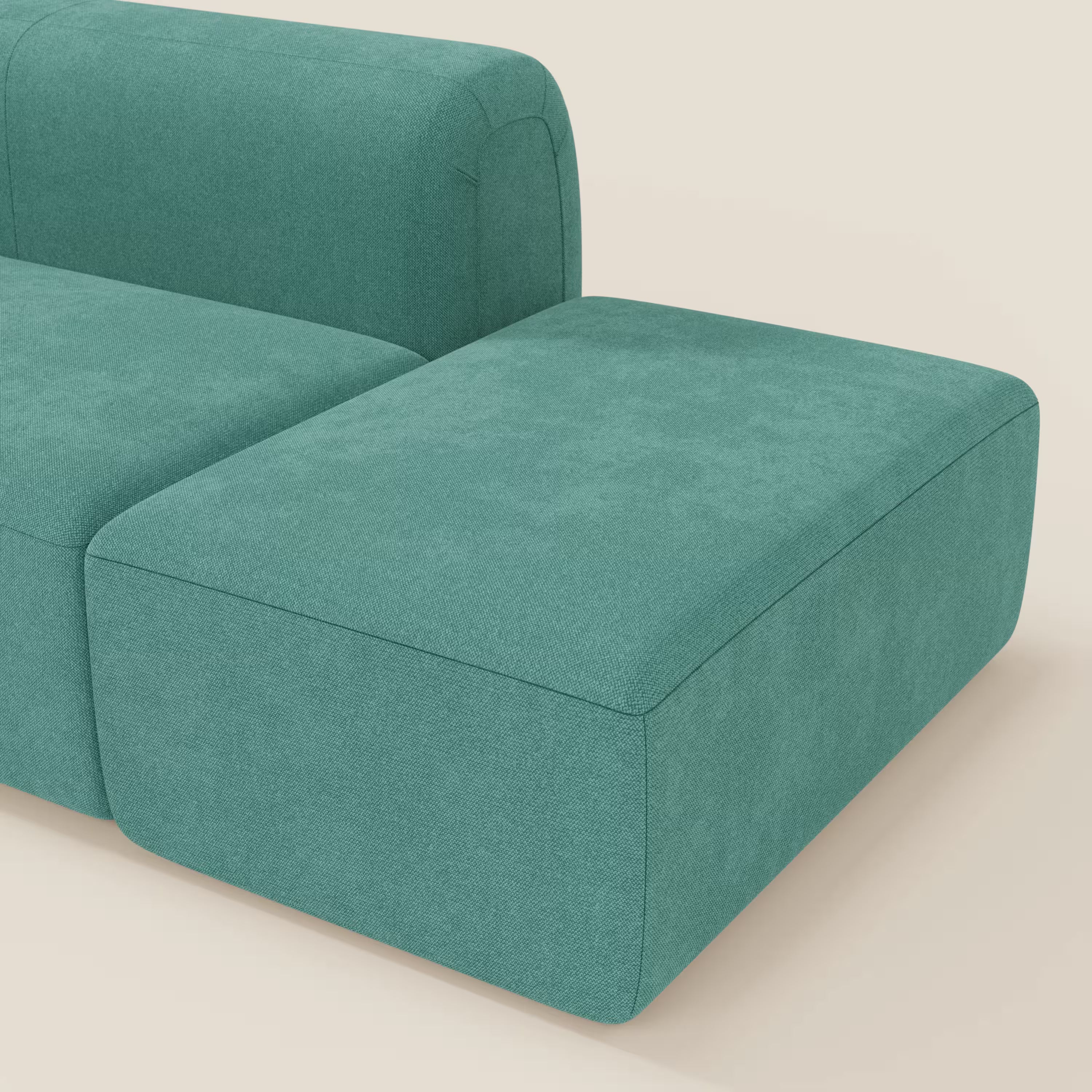 Il BonBon Divano componibile di Divani.Store è caratterizzato da uno schienale basso e da un ampio pouf terminale in smacchiabile T23 verde acqua, con angoli arrotondati e morbidi e tessuto opaco, su uno sfondo beige chiaro.