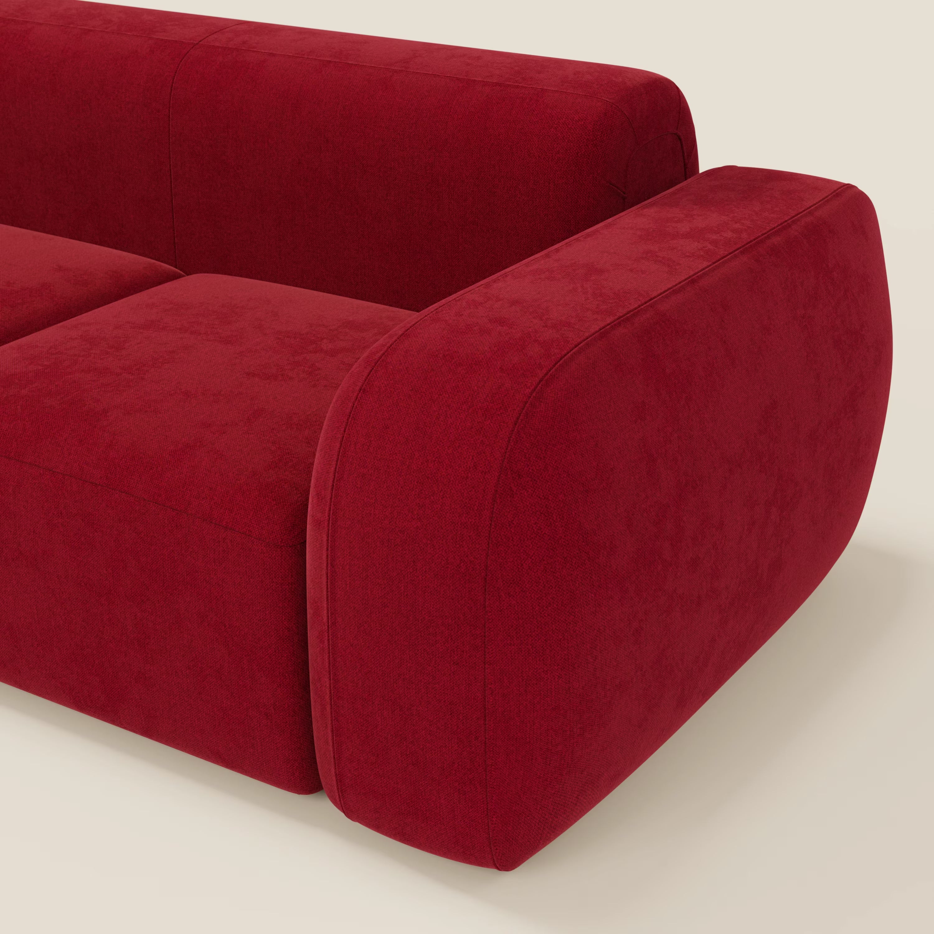 Un primo piano del BonBon Divano modulare componibile - Composizione Spaccamattone di Divani.Store in smacchiabile T23 bordeaux mostra il bracciolo e lo schienale morbidi e arrotondati, caratterizzati da un design minimalista unico su uno sfondo beige chiaro.