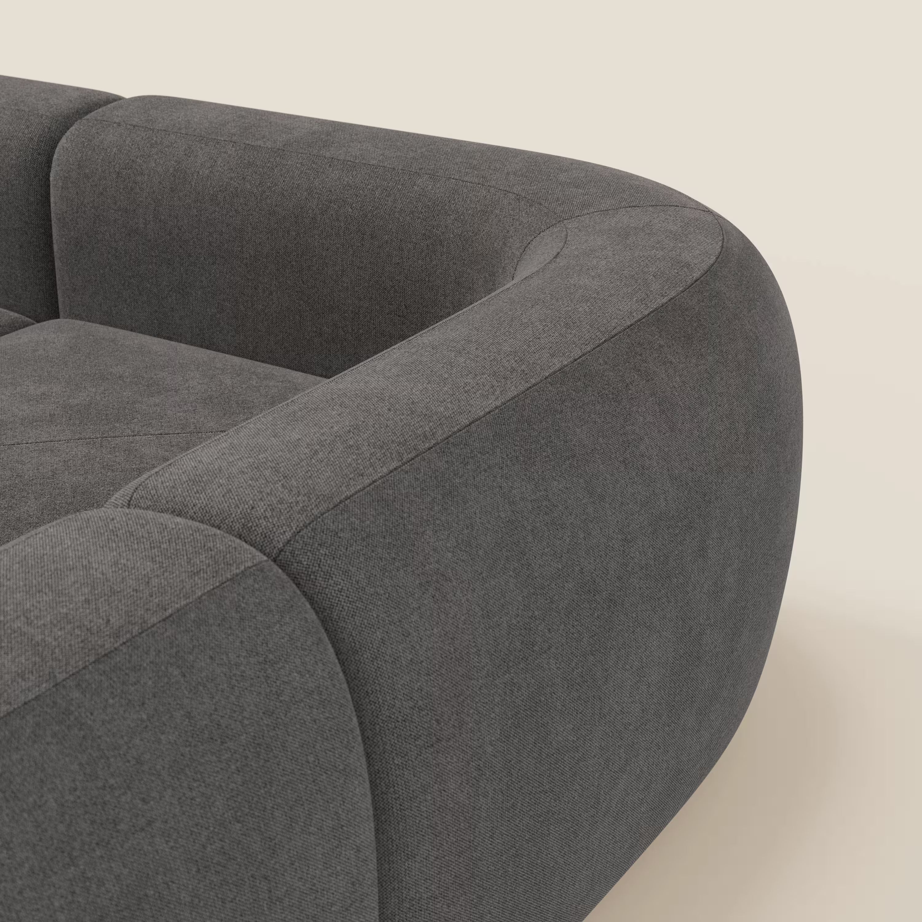 Primo piano del divano angolare componibile e modulare BonBon di Divani.Store in tessuto smacchiabile T23 antracite. I suoi bordi morbidi e arrotondati e il suo design minimalista spiccano sullo sfondo beige chiaro, mettendo in risalto i suoi contorni slanciati.