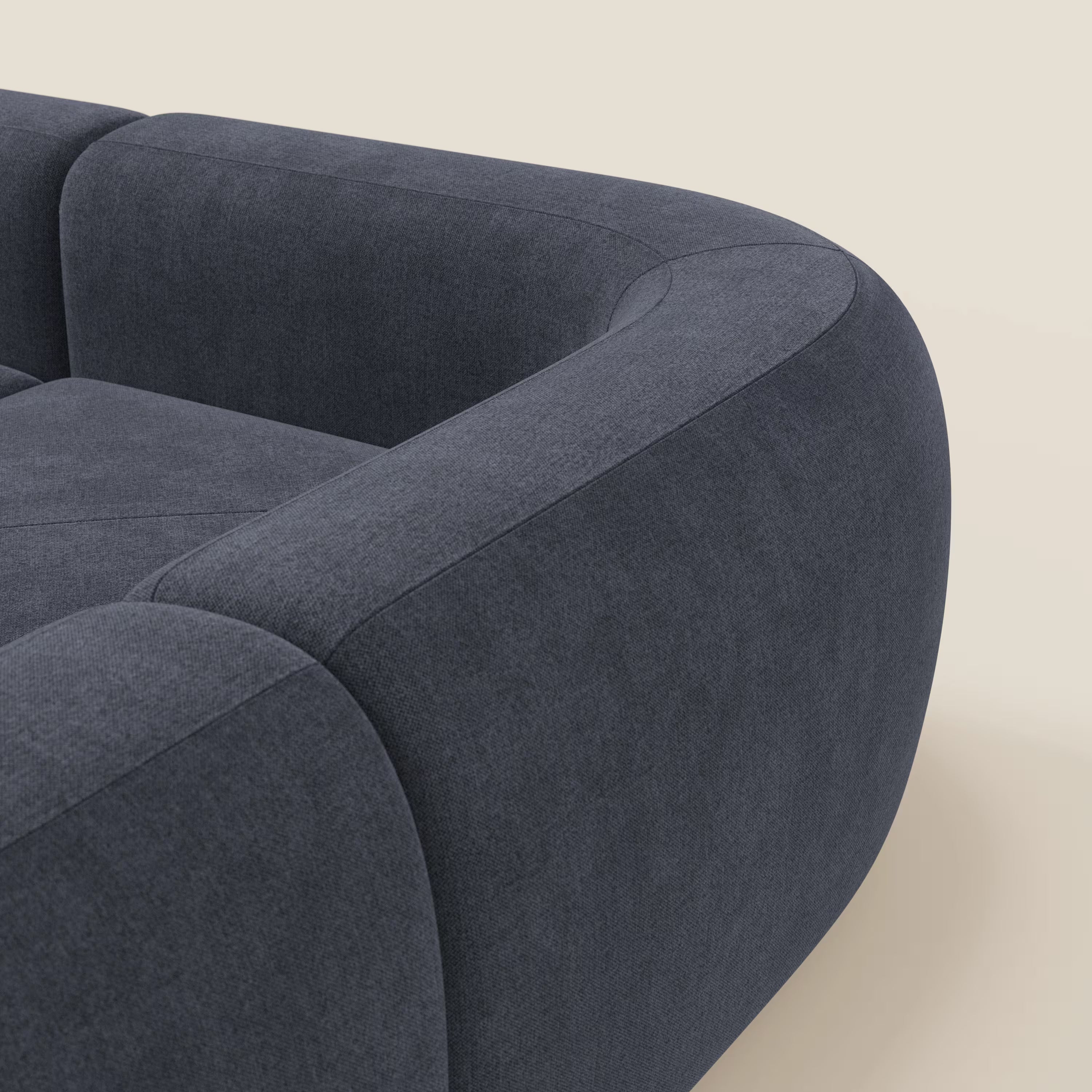Primo piano del divano angolare componibile e modulare BonBon di Divani.Store in tessuto smacchiabile T23 blu ardesia, caratterizzato da cuscini morbidi, braccioli lisci e curvi e un design minimalista su uno sfondo beige chiaro.