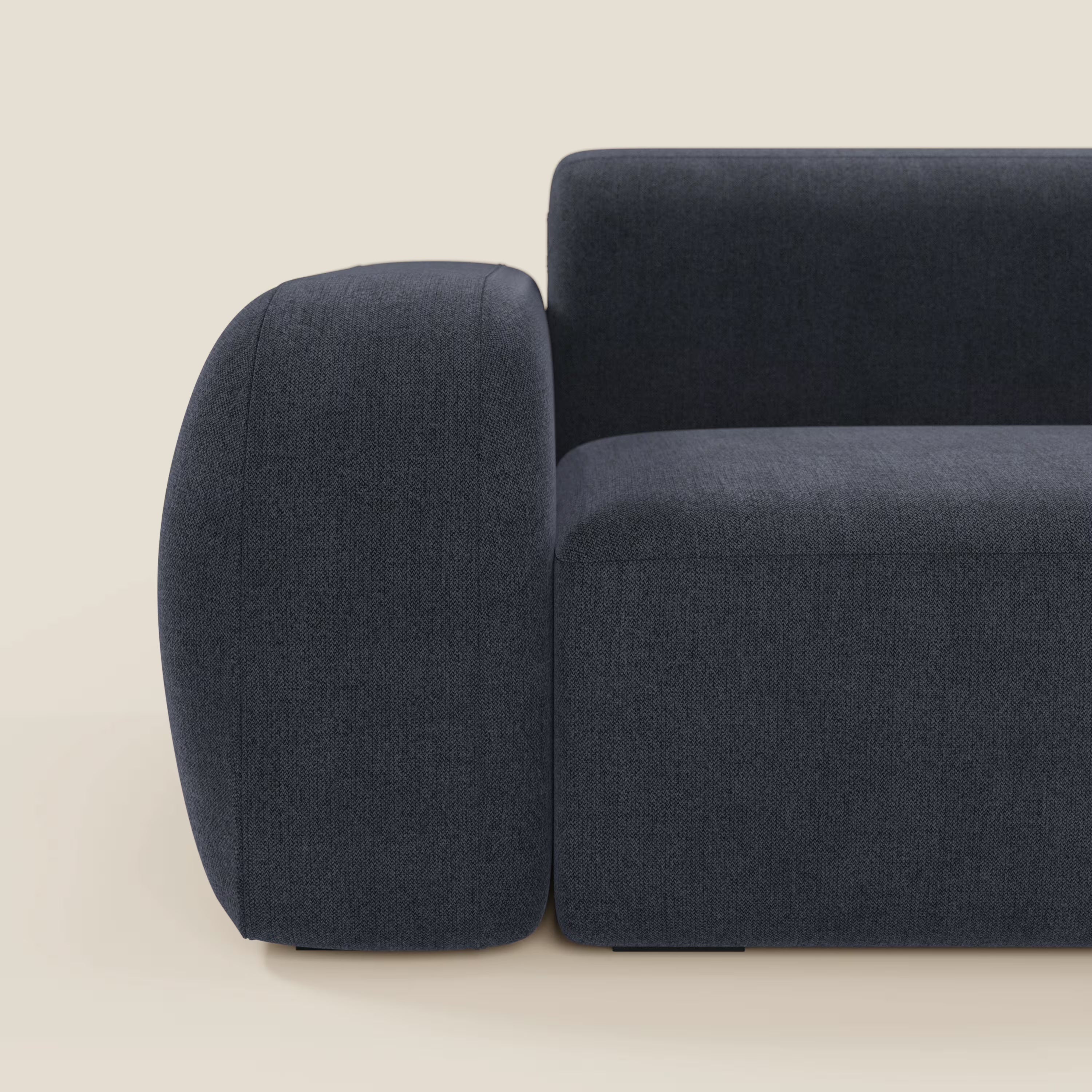 Primo piano del divano angolare componibile e modulare BonBon di Divani.Store in tessuto smacchiabile T23 blu ardesia, che mostra solo il bracciolo, la seduta e parte dello schienale su uno sfondo beige chiaro.