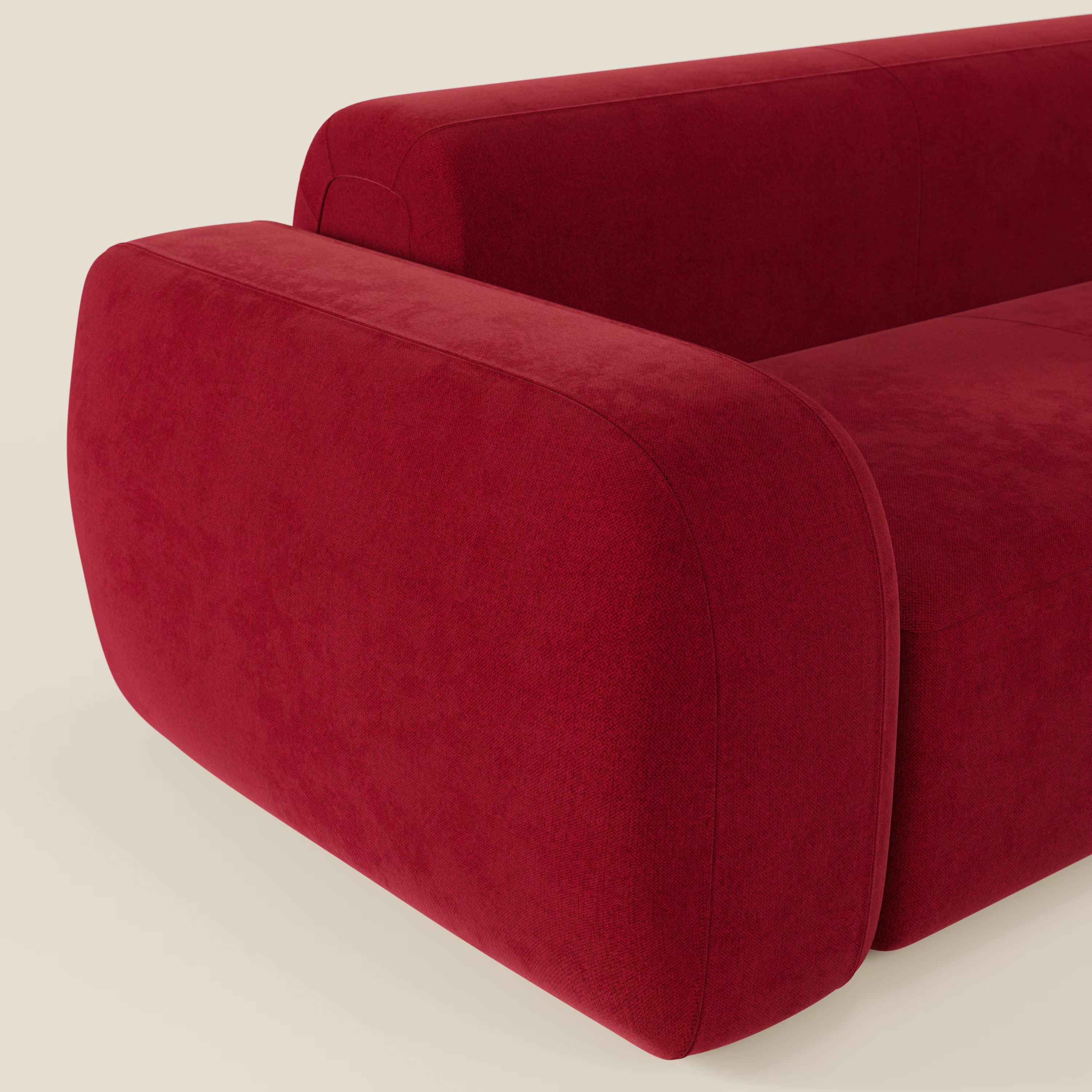 Primo piano del divano angolare componibile e modulare BonBon di Divani.Store in smacchiabile T23 bordeaux, caratterizzato da braccioli oversize arrotondati e linee pulite per un look contemporaneo e su misura su uno sfondo semplice.