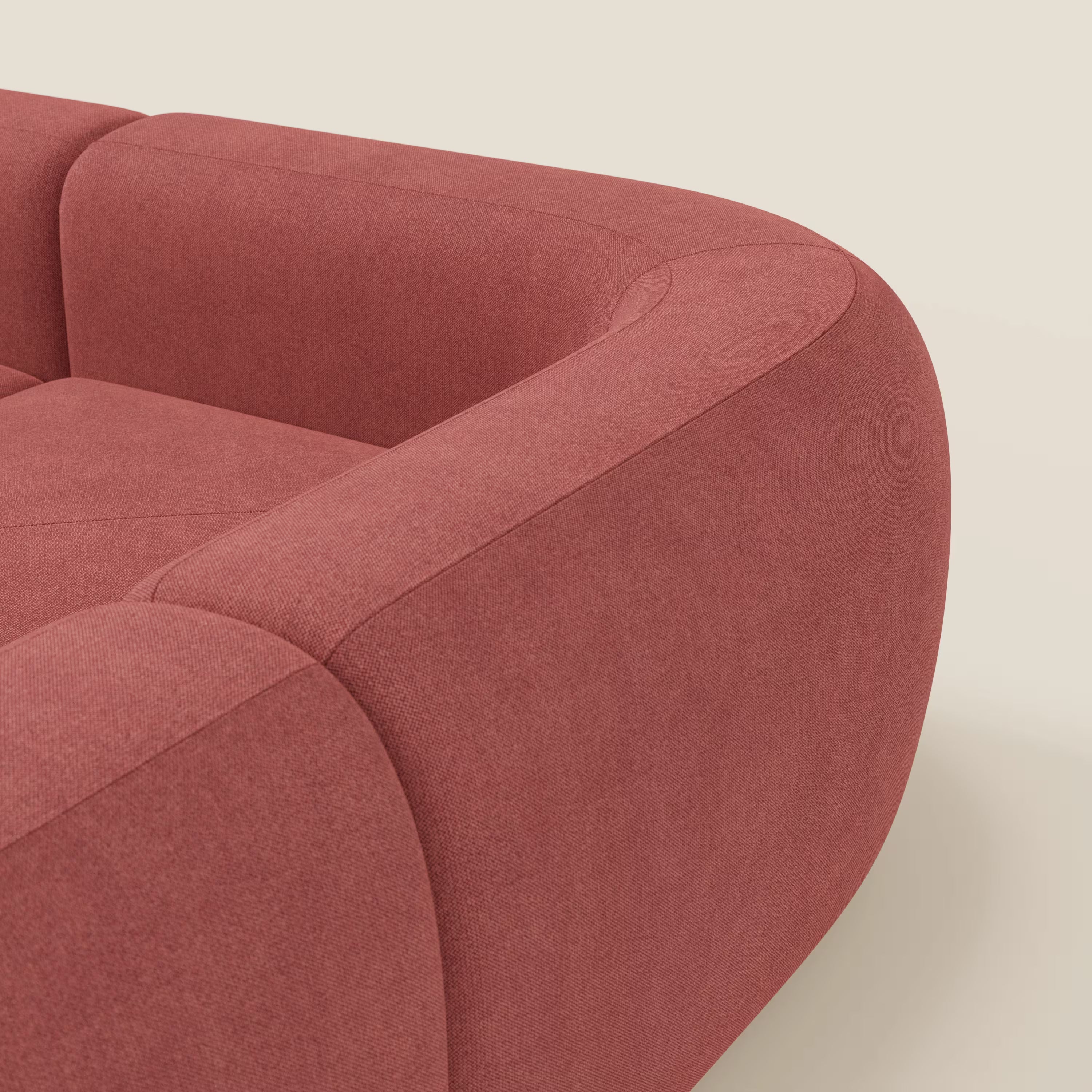 Un primo piano del divano angolare componibile e modulare BonBon di Divani.Store mostra i suoi bordi morbidi e arrotondati in tessuto smacchiabile T23 rosso ciliegia, con uno sfondo bianco sporco che ne accentua l'artigianalità italiana e il design moderno.
